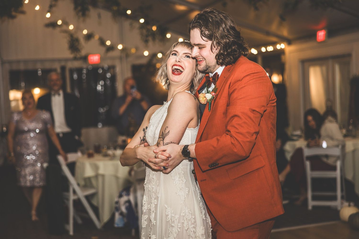 Guests dance and celebrate at an indoor wedding reception with ambient lighting.