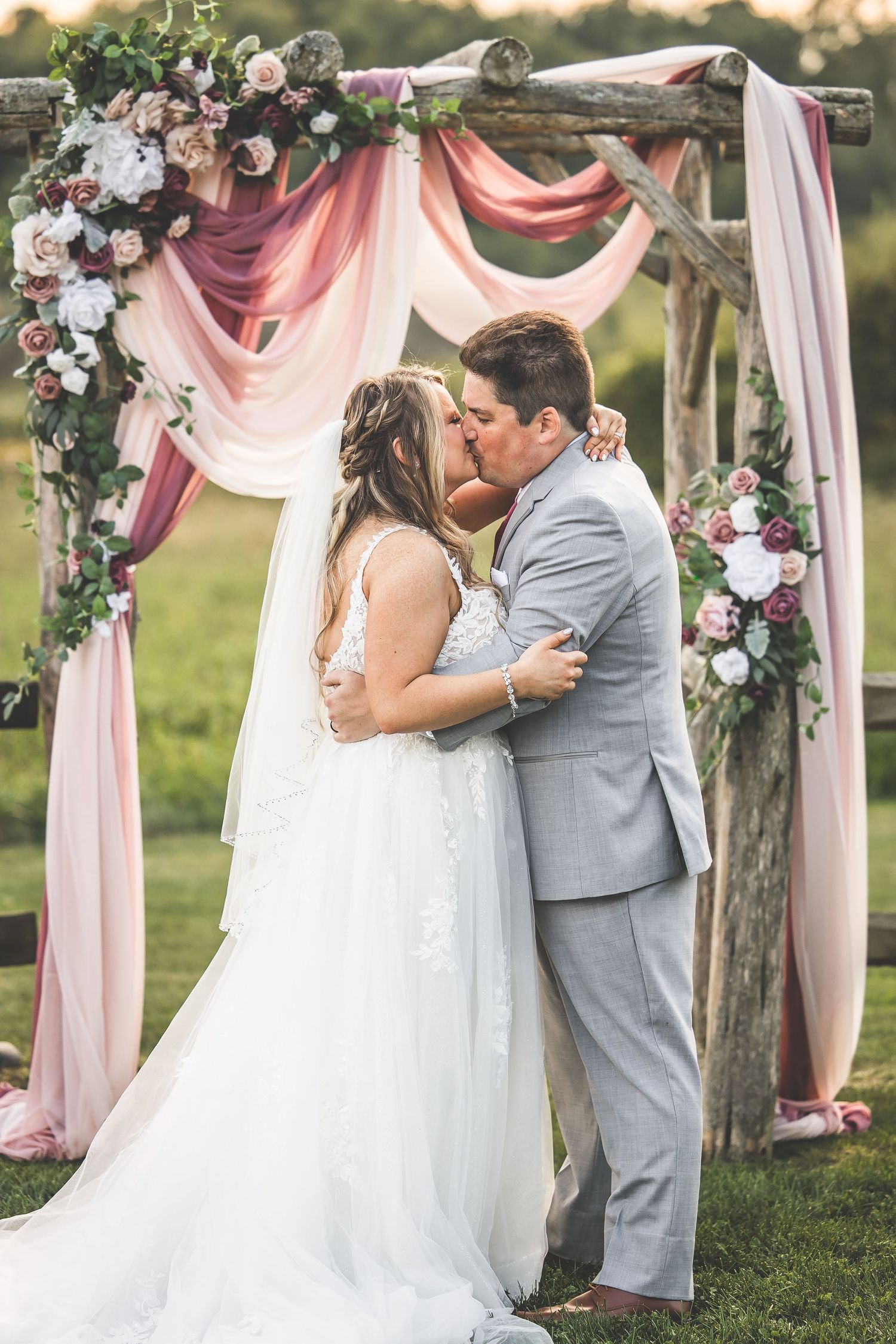 Series of romantic moments during outdoor wedding ceremony under floral arch with pink drapery.