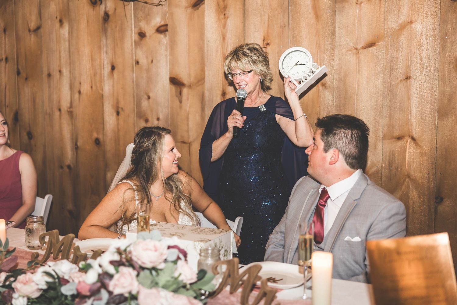 Wedding reception guests enjoying speeches and toasts in rustic barn venue with string lights.
