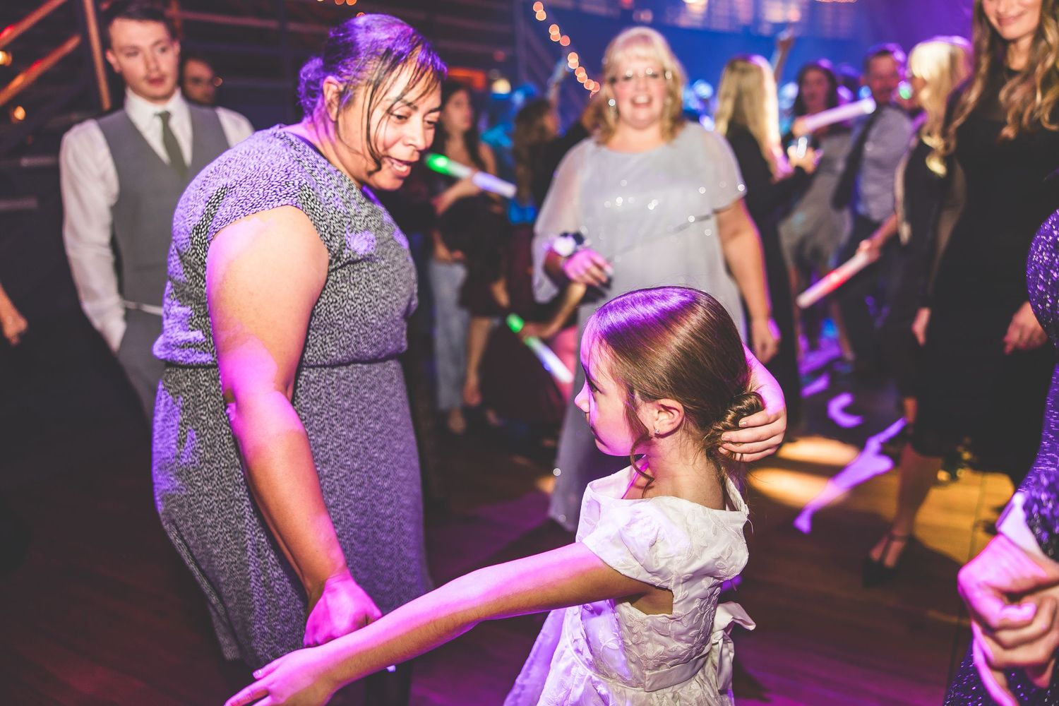 Guests dancing and celebrating on a dance floor illuminated by purple and blue lighting.