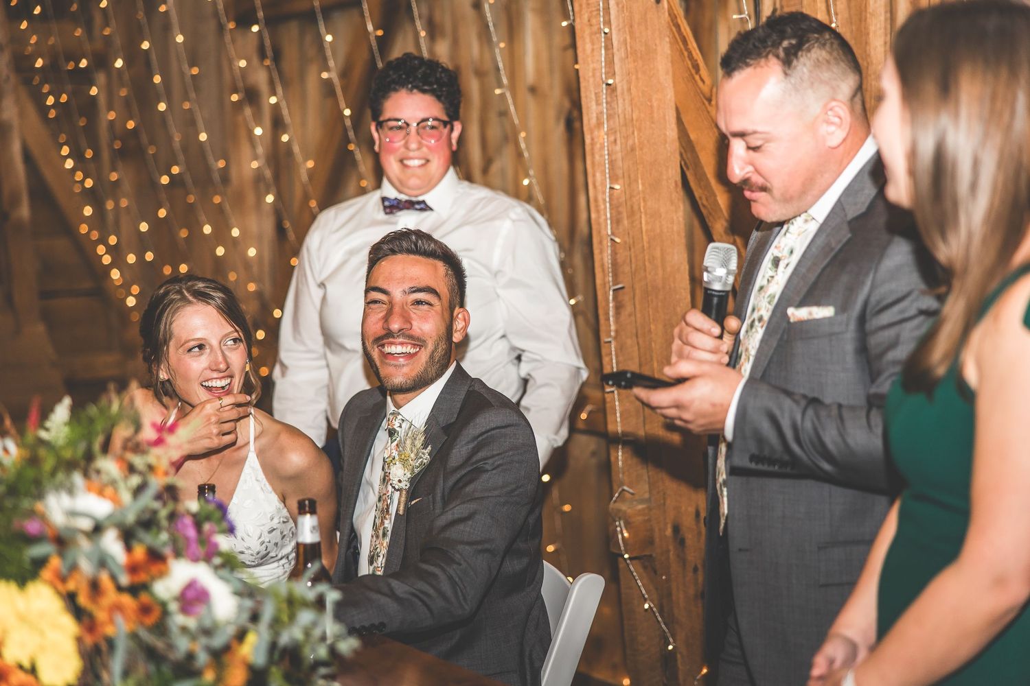 Wedding reception guests enjoying festivities inside a rustic barn venue with twinkle lights.