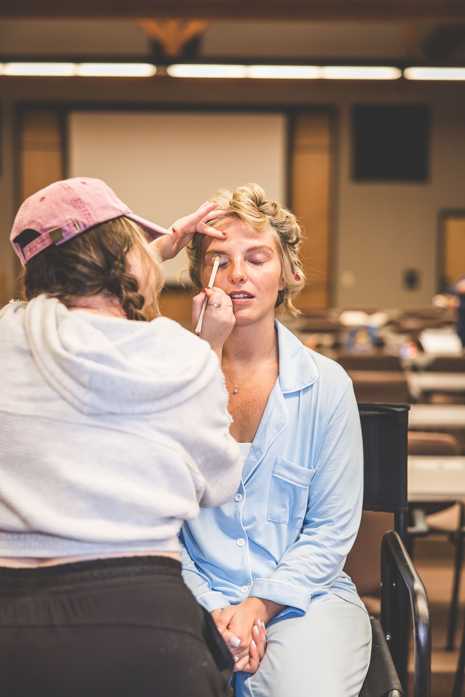 Makeup artist applies cosmetics during wedding preparation in a dressing room.