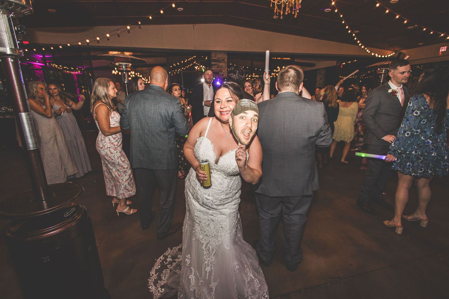 Wedding guests dancing at a reception under string lights in a dimly lit venue.