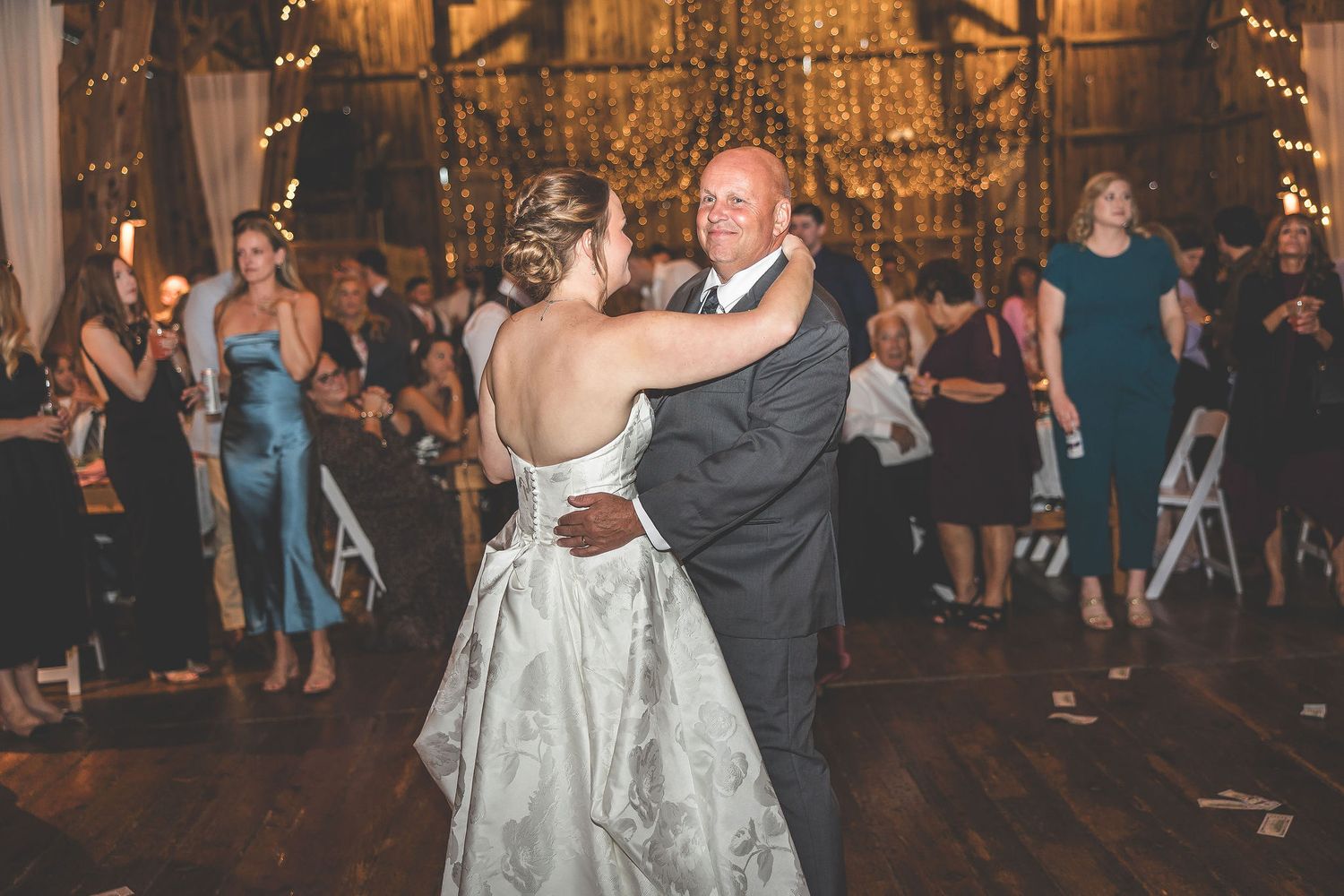 Wedding reception dance in rustic barn venue with hanging chandelier and guests watching.