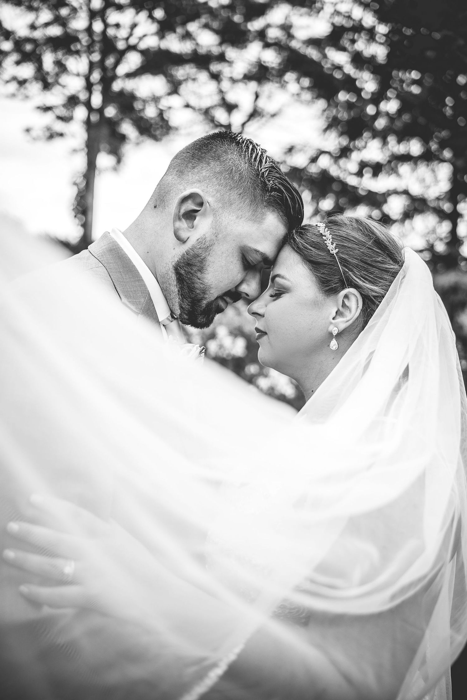 A romantic black and white wedding photo with a flowing veil creating a dreamy effect in an outdoor setting.