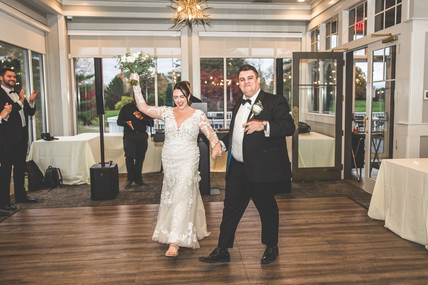 Wedding party dances together in an elegant venue with hardwood floors and chandeliers overhead.