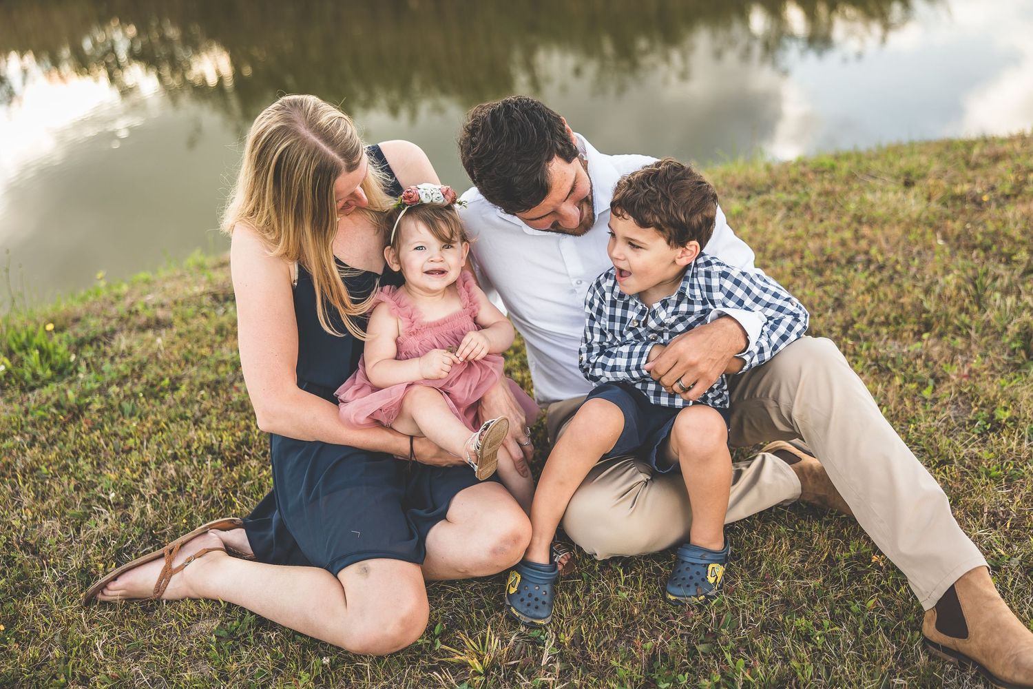 Family relaxing together on grassy hill beside a peaceful lake.