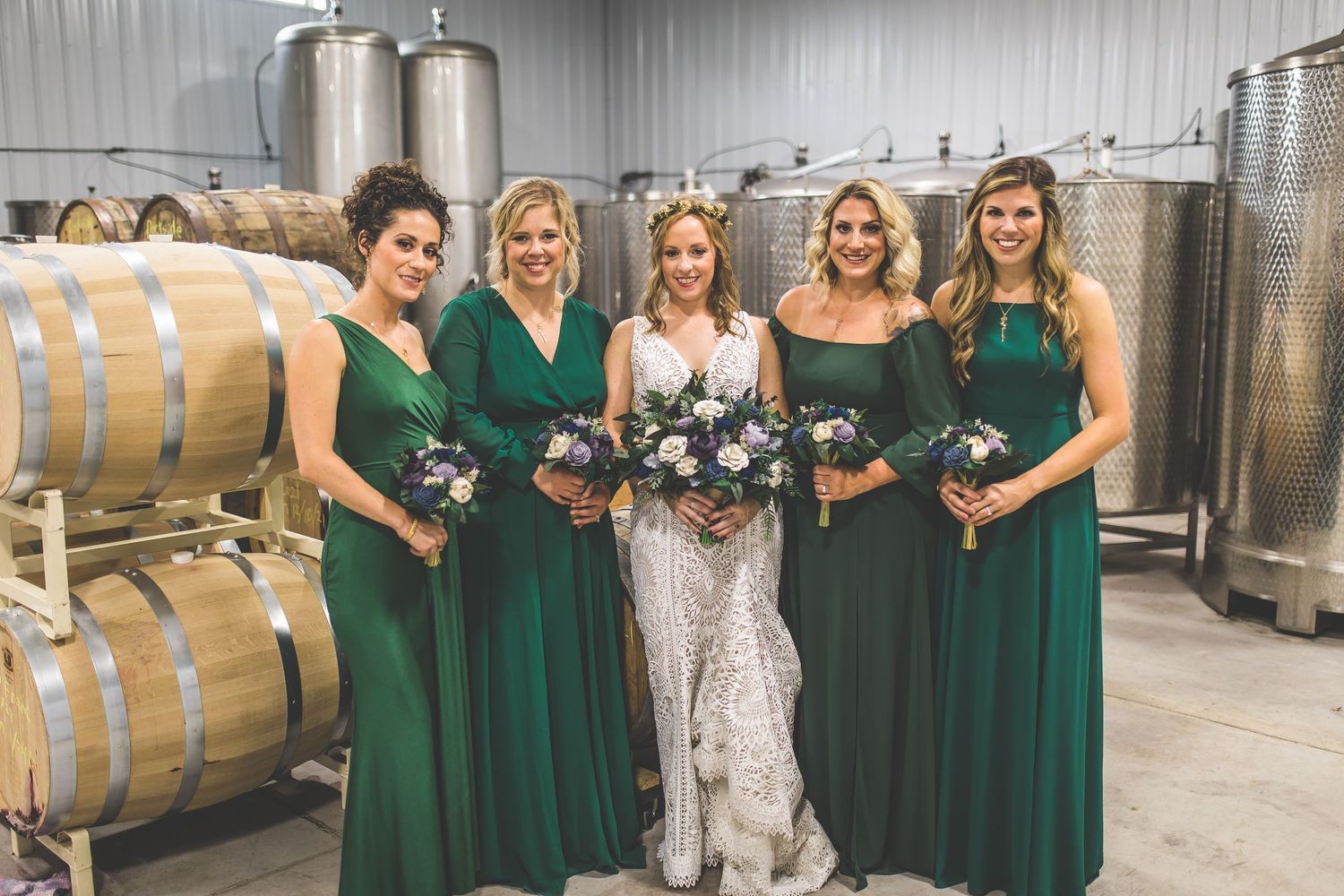 Wedding party wearing emerald green dresses poses in winery cellar.