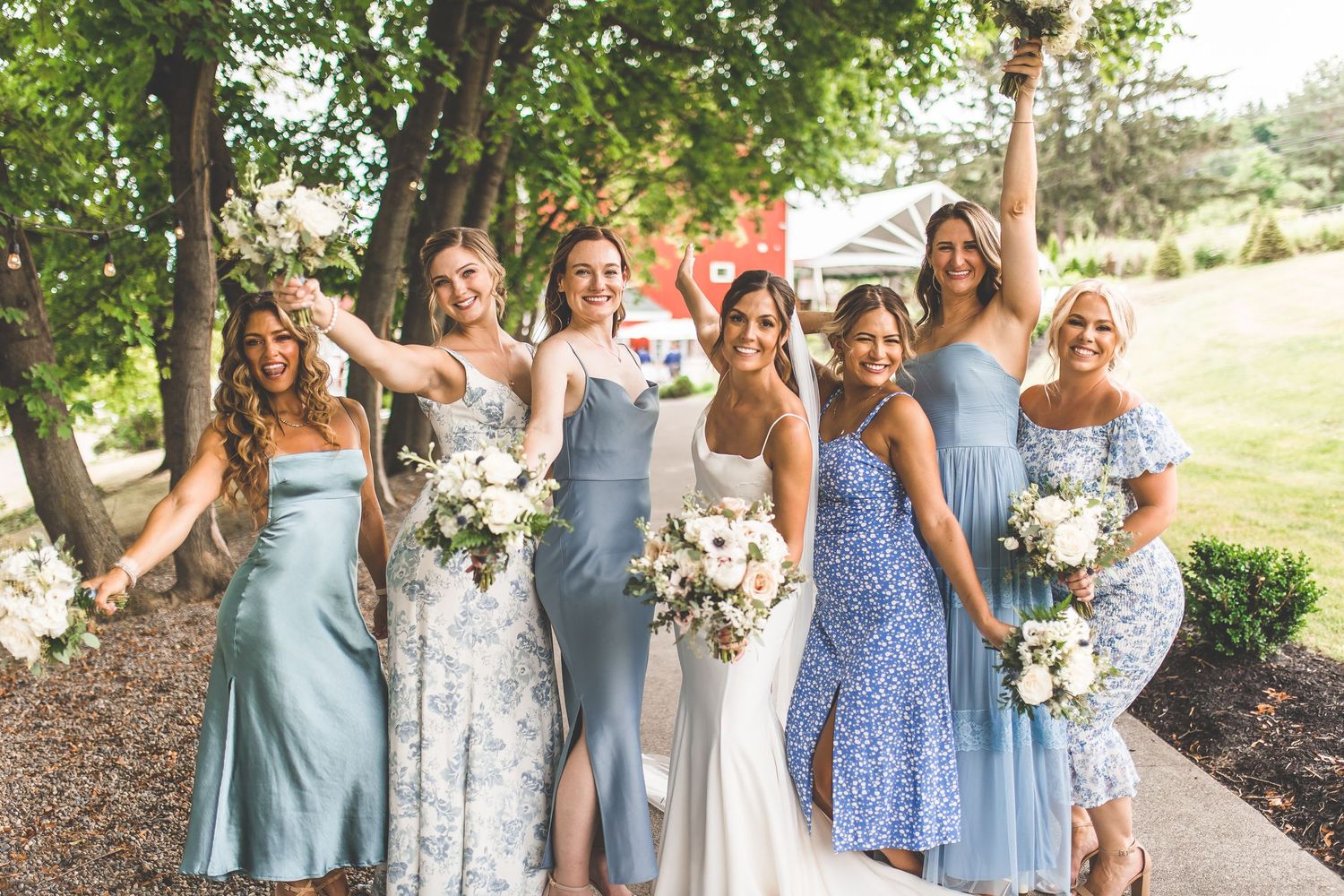 Bridesmaids in light blue and floral print dresses gather for a group photo in natural setting.