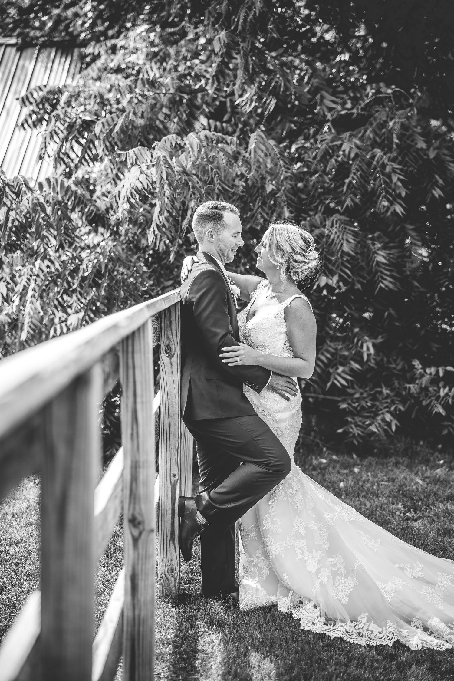 A black and white intimate moment between newlyweds on a wooden bridge surrounded by trees.