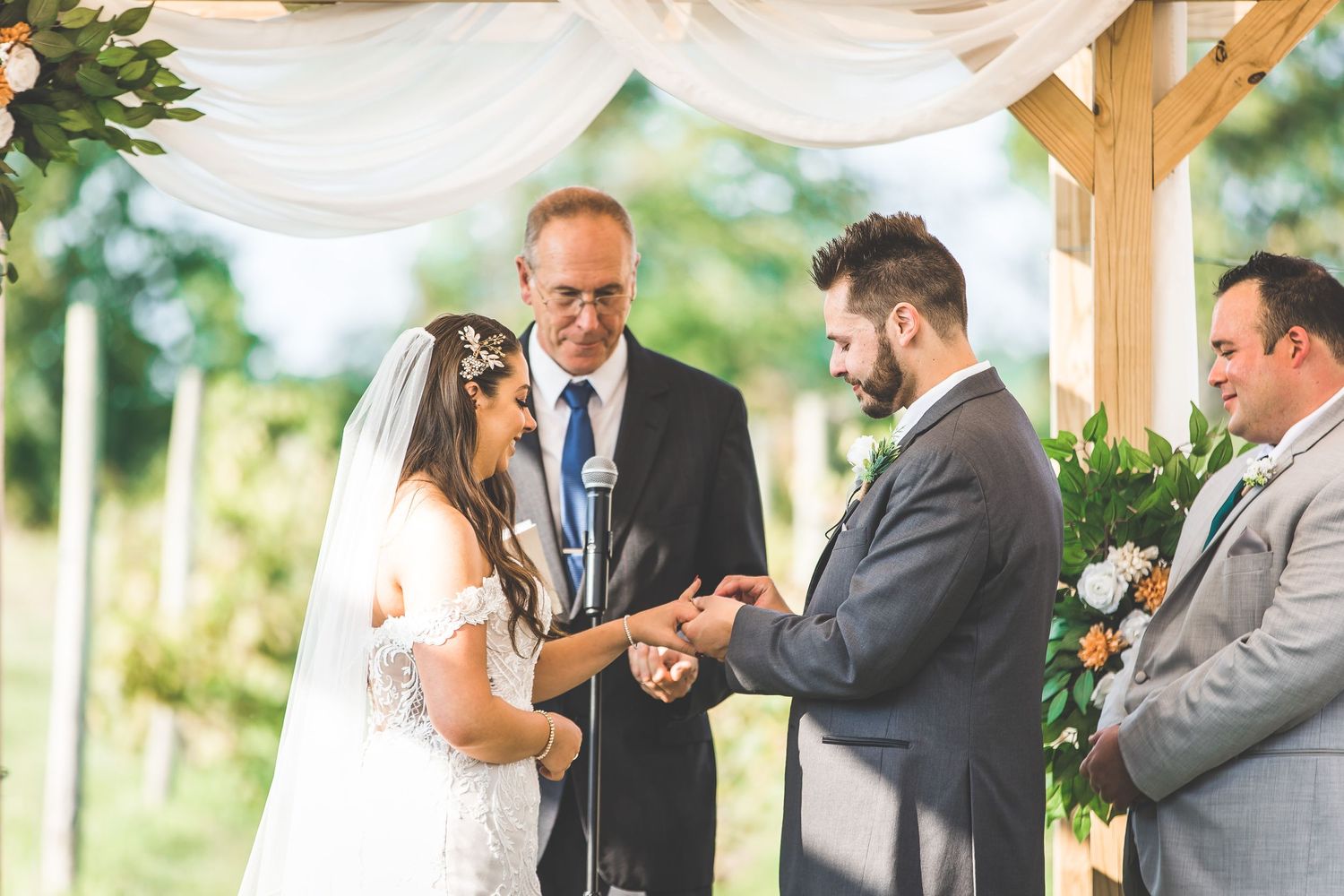 Wedding ceremony with couple exchanging vows under draped wooden pergola with floral accents.