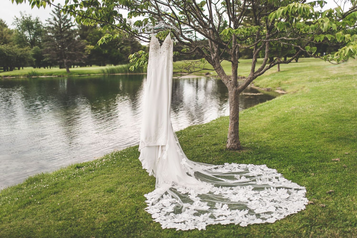 Beautiful wedding dress train spread out on green grass near a serene lake.