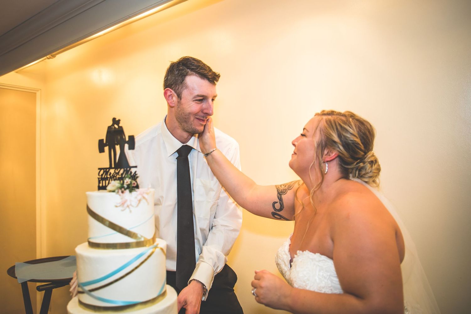 Wedding couple sharing a fun moment with cake at indoor reception.