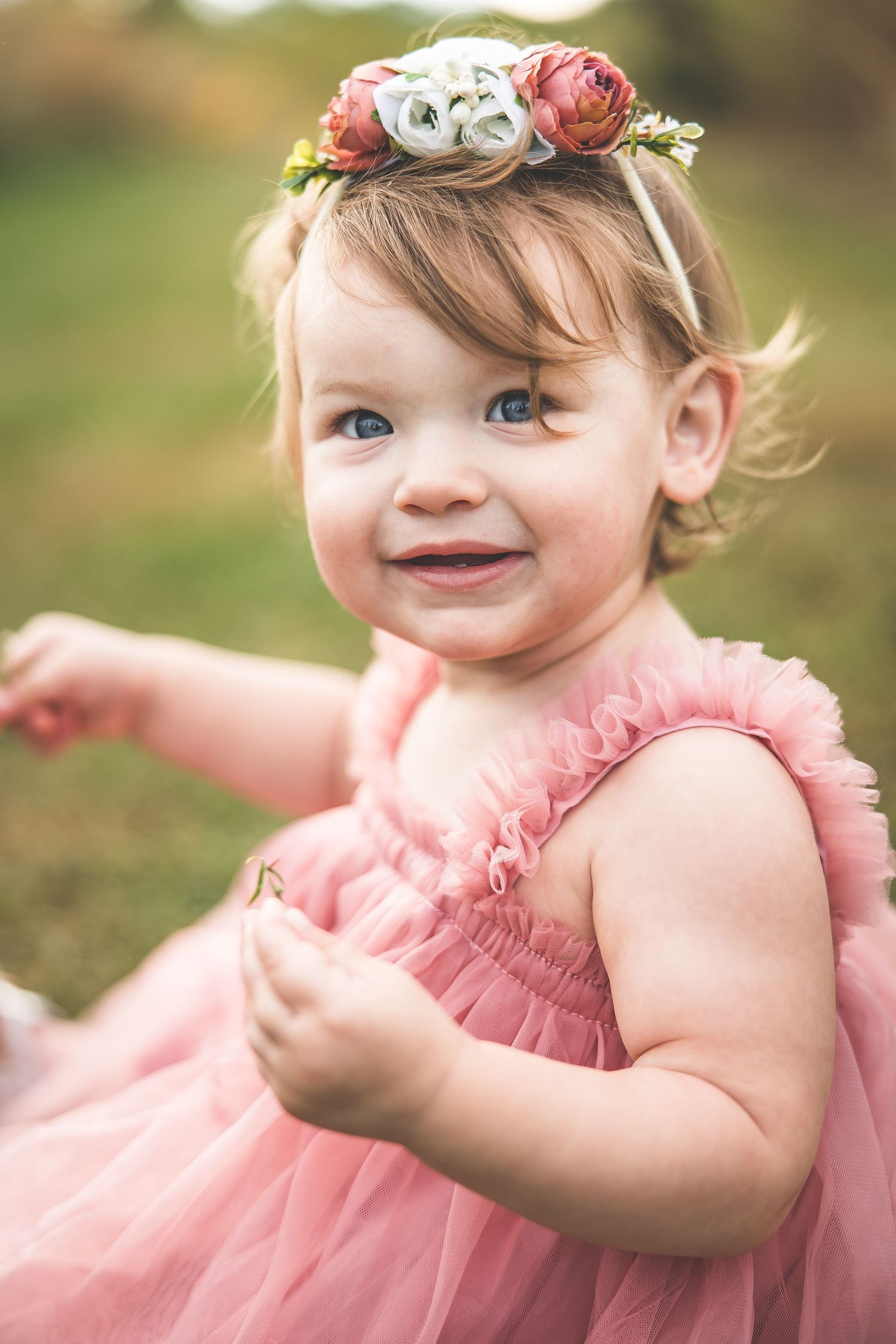 Young child wearing a pink tulle dress and floral crown in an outdoor setting.