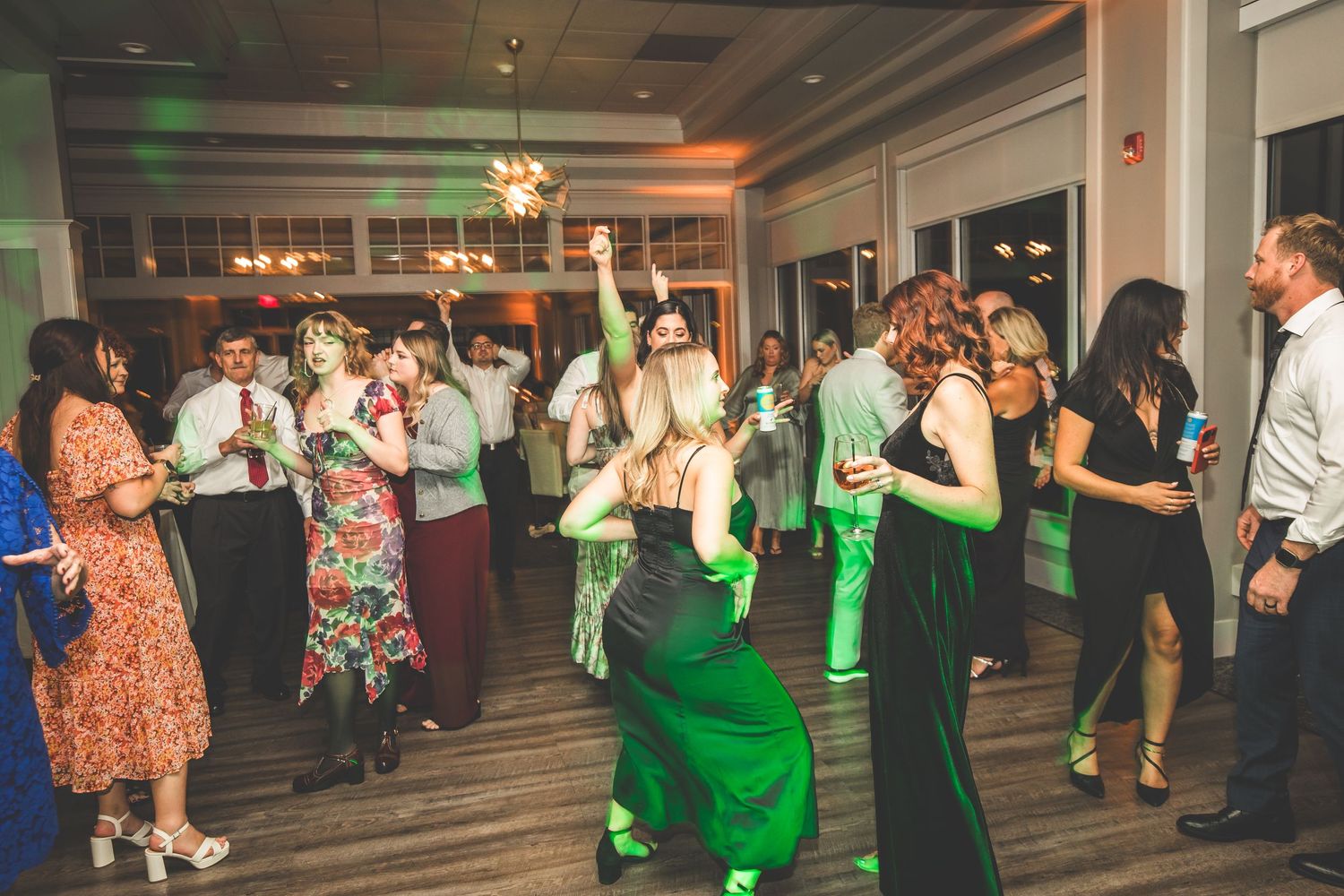 Wedding party guests dancing in a spacious venue with mood lighting and decorations.