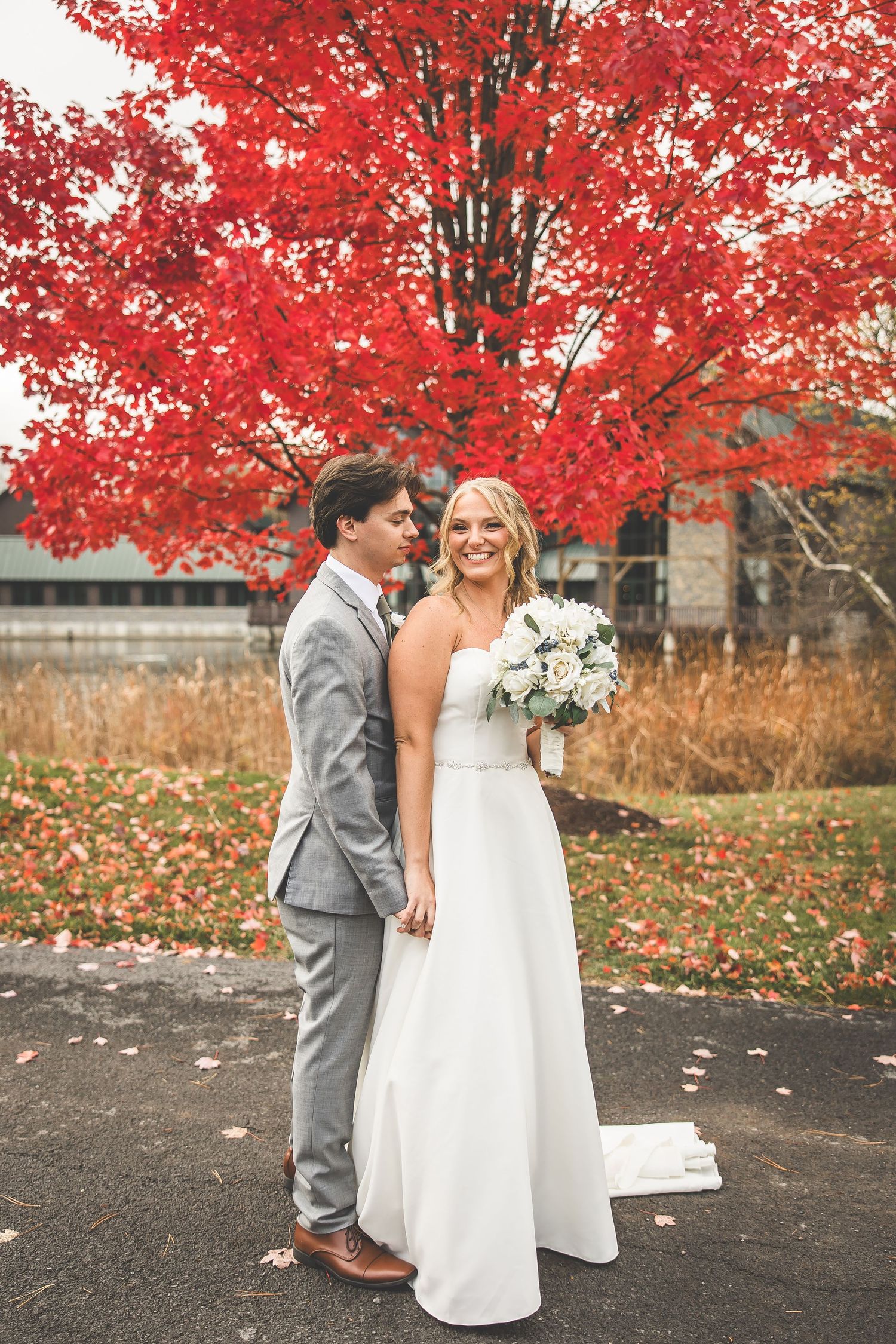 Newlyweds share romantic moment beneath bright red fall foliage.