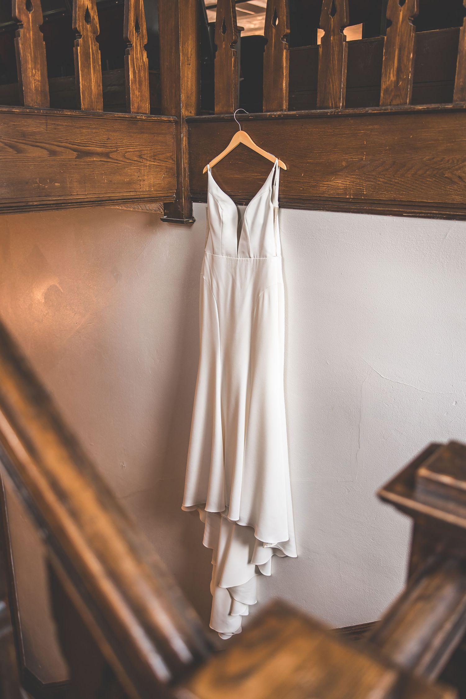 White wedding dress hanging against rustic wooden wall in natural light.