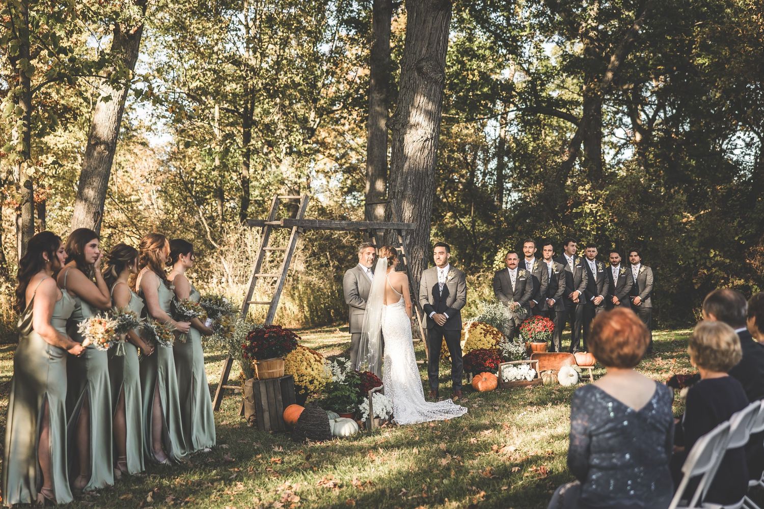Wedding ceremony in progress with bridesmaids in sage dresses and fall decorations.