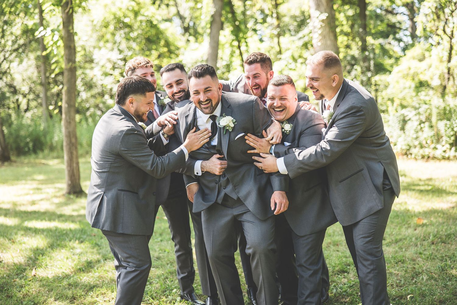 Groomsmen in grey suits share a candid laughing moment during outdoor wedding photos.