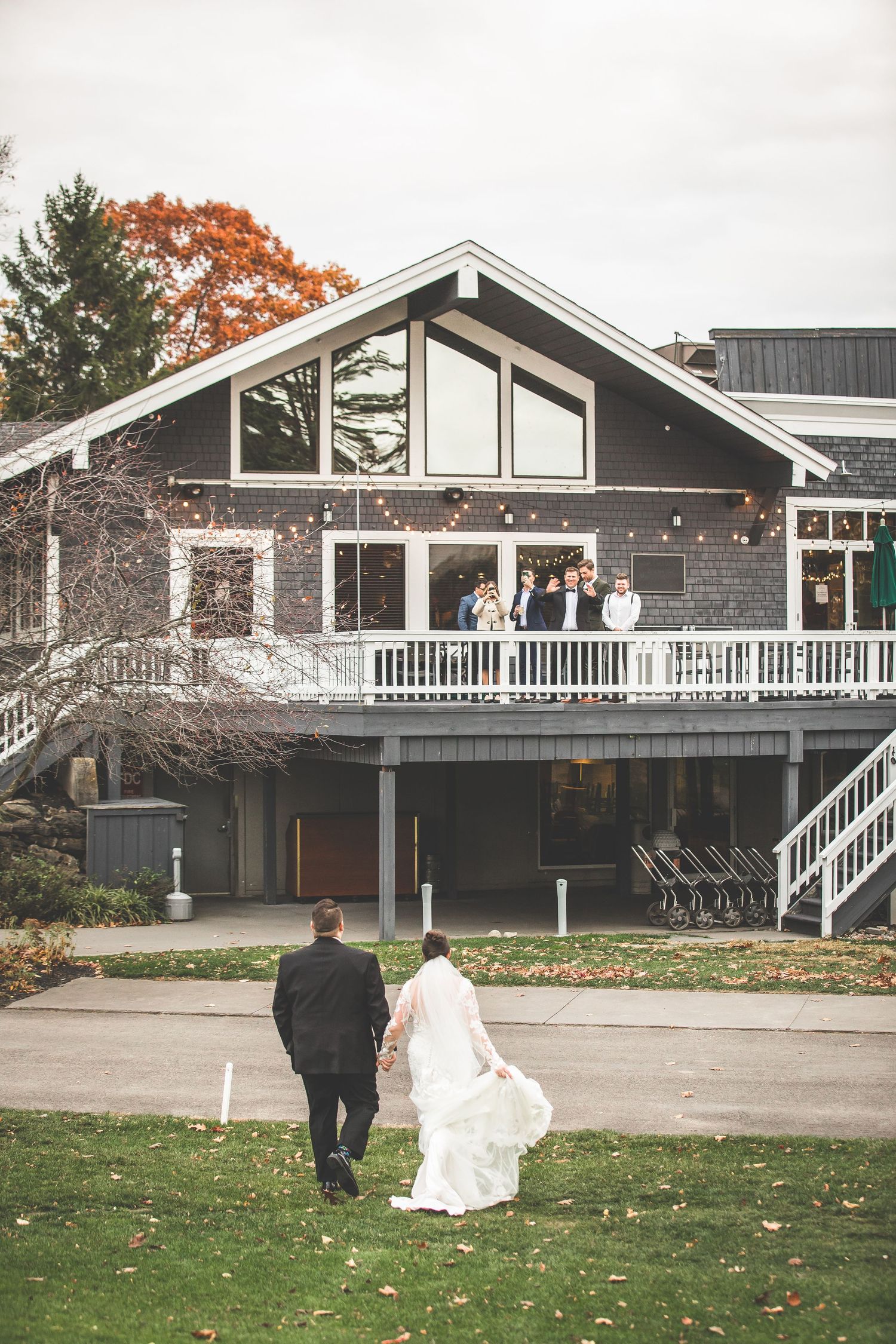 Couple walks towards modern venue building with white railings and autumn leaves on ground.