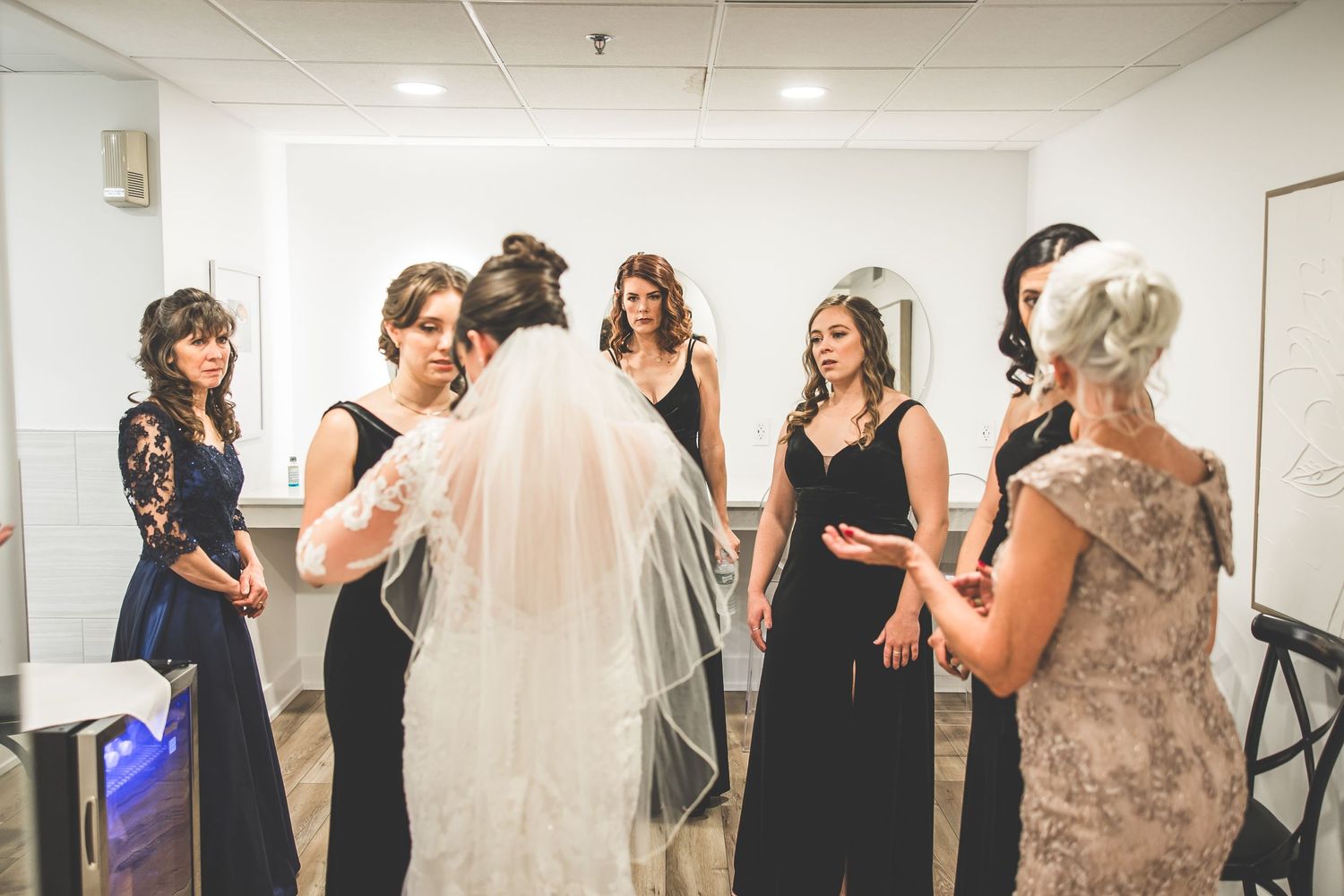 Wide angle view of bridesmaids in black dresses gathered in a bright indoor space.