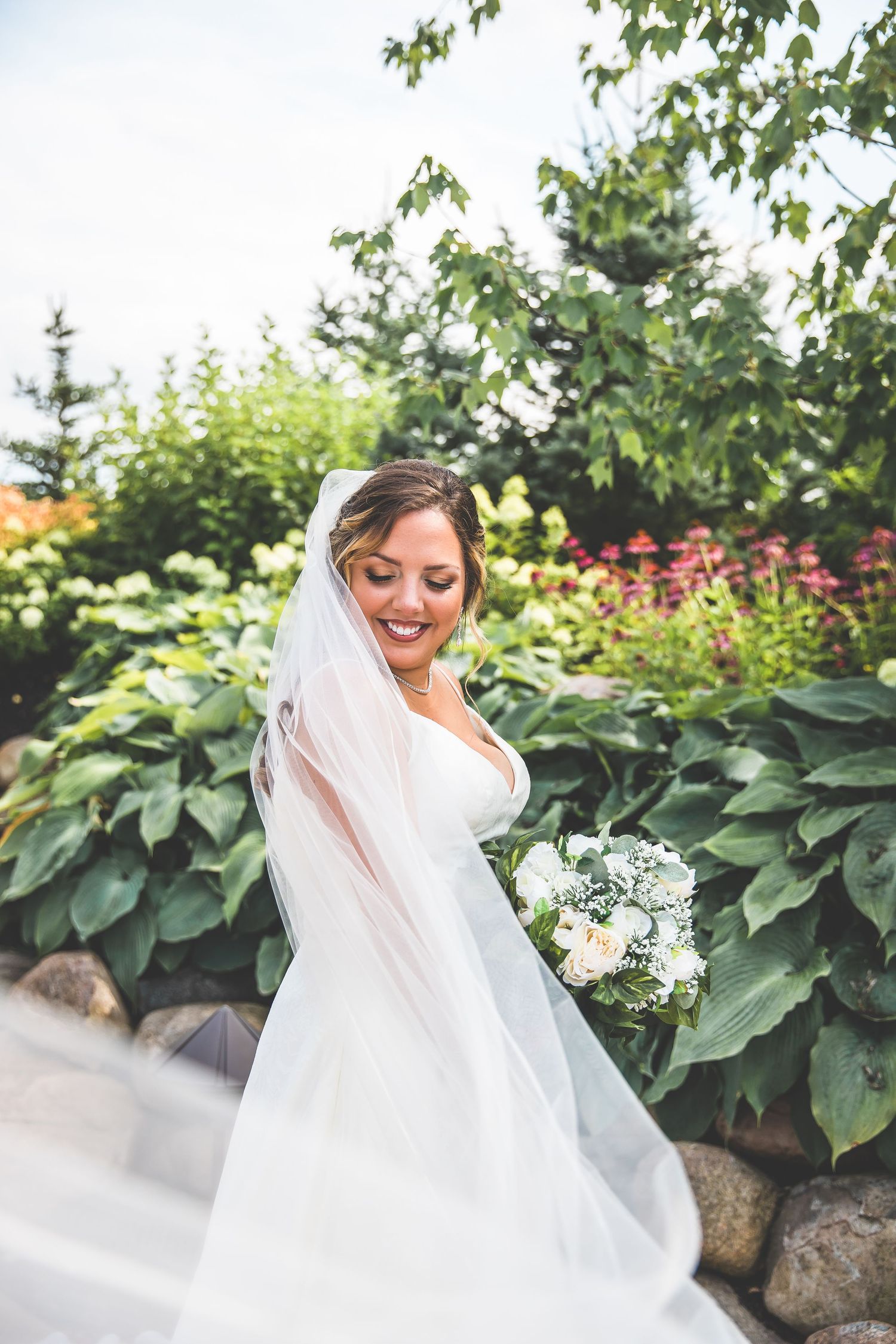 A flowing white wedding veil catches the breeze in a garden setting with blooming flowers.