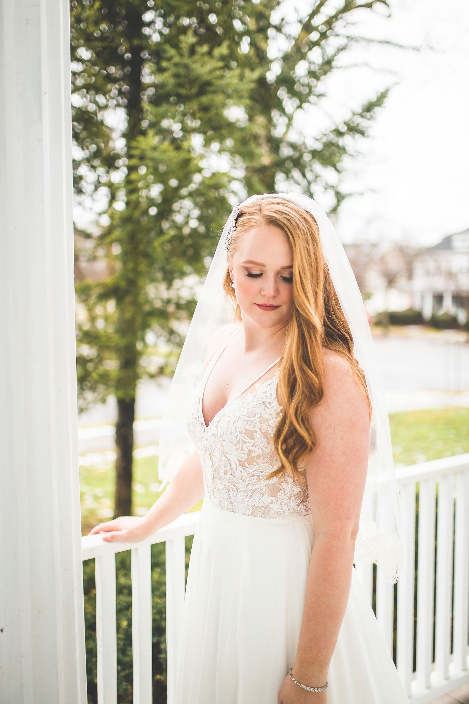 Elegant bride in lace dress poses on white porch with classic architectural details.