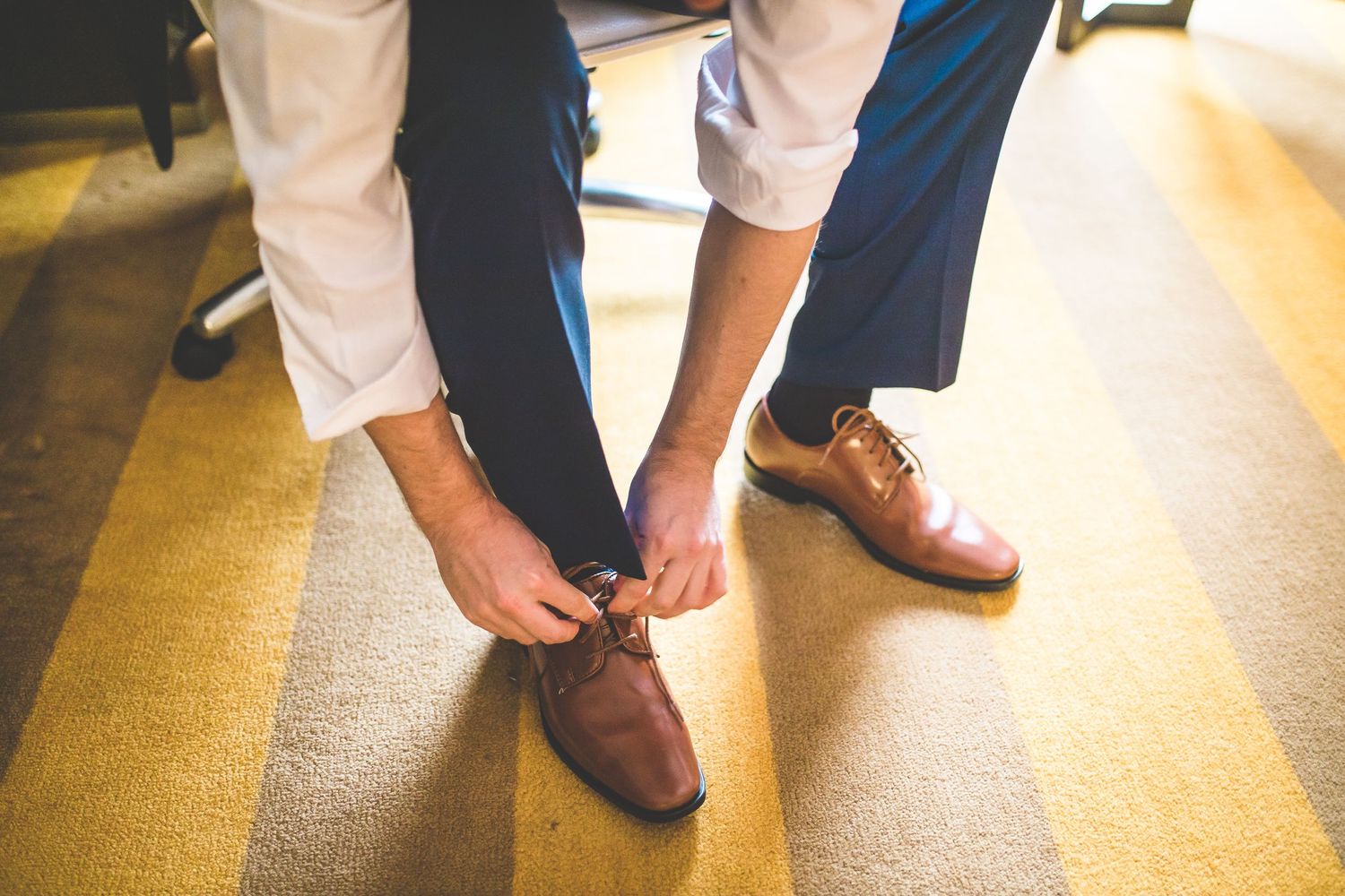 Person tying brown leather dress shoes on golden floor.