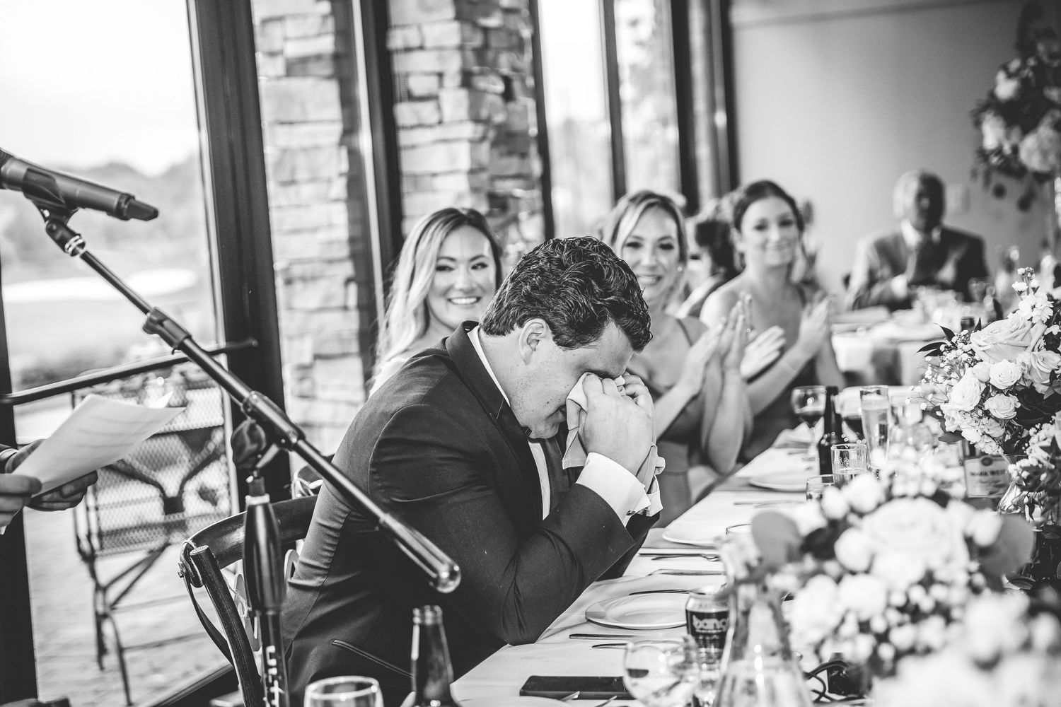 Wedding party members react emotionally during reception speeches at an elegant venue.