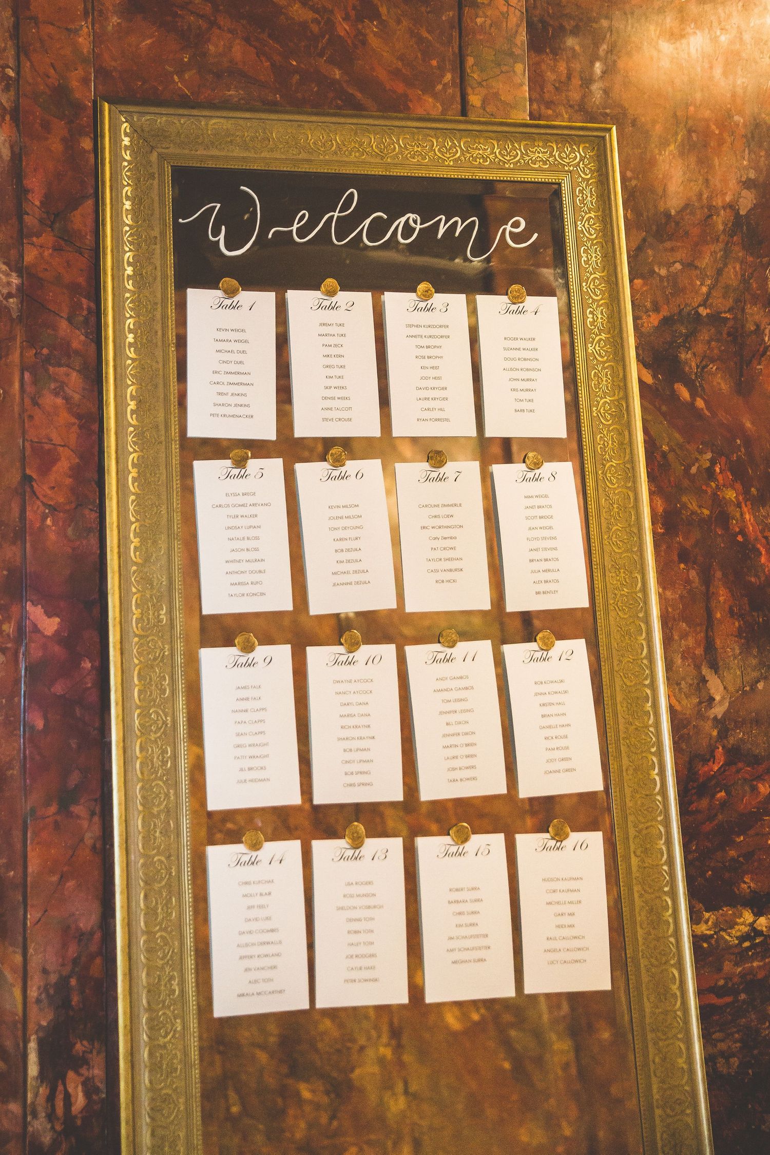 Wedding seating chart displayed in an ornate gold frame with paper name cards.