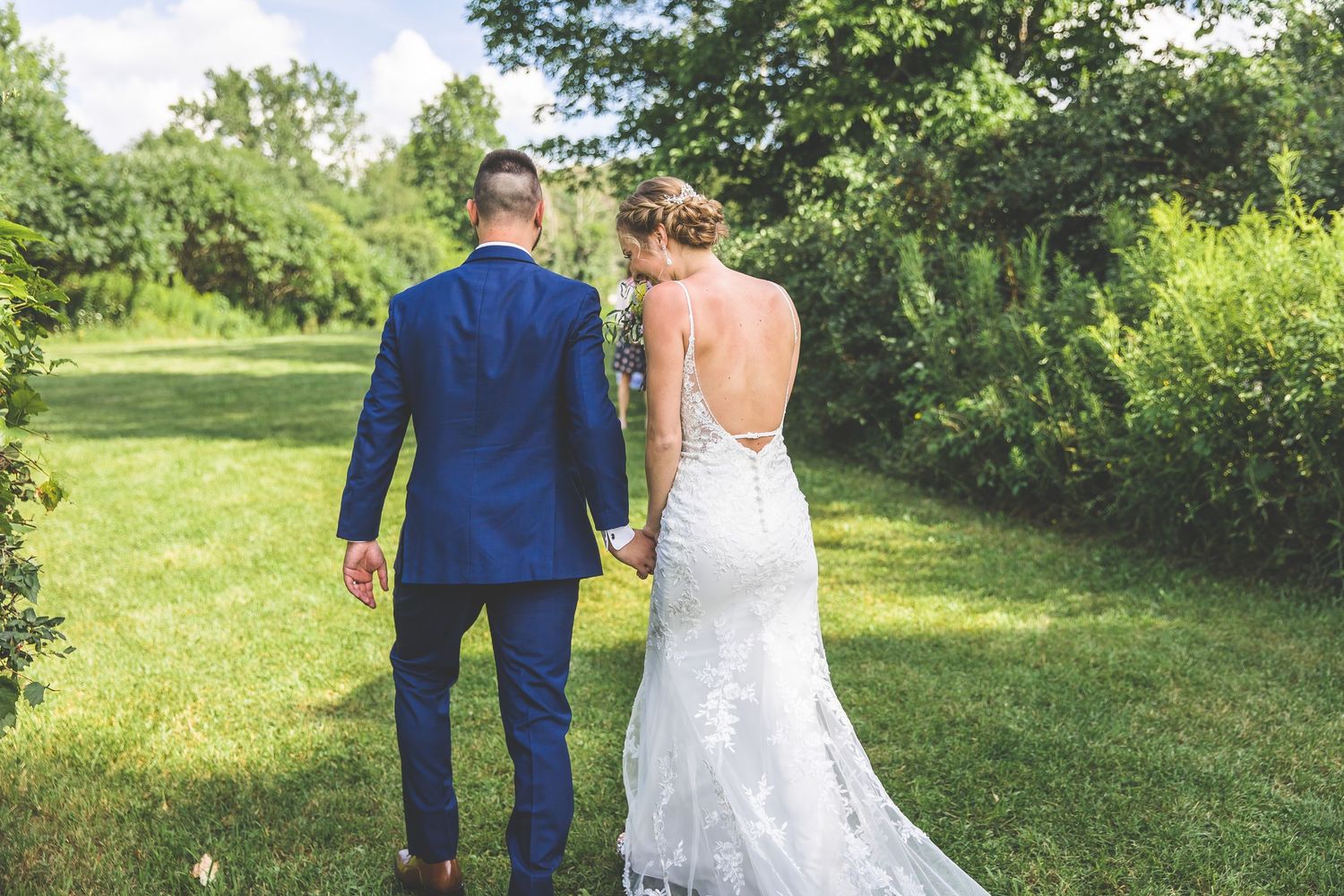 Wedding couple and wedding party pose together under wooden arch in sunny outdoor garden setting.