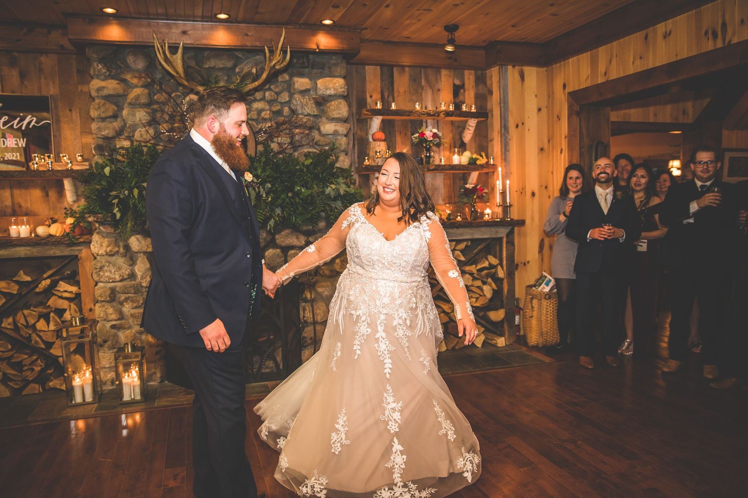 Newlyweds dance surrounded by guests in a cozy rustic venue with stone walls.