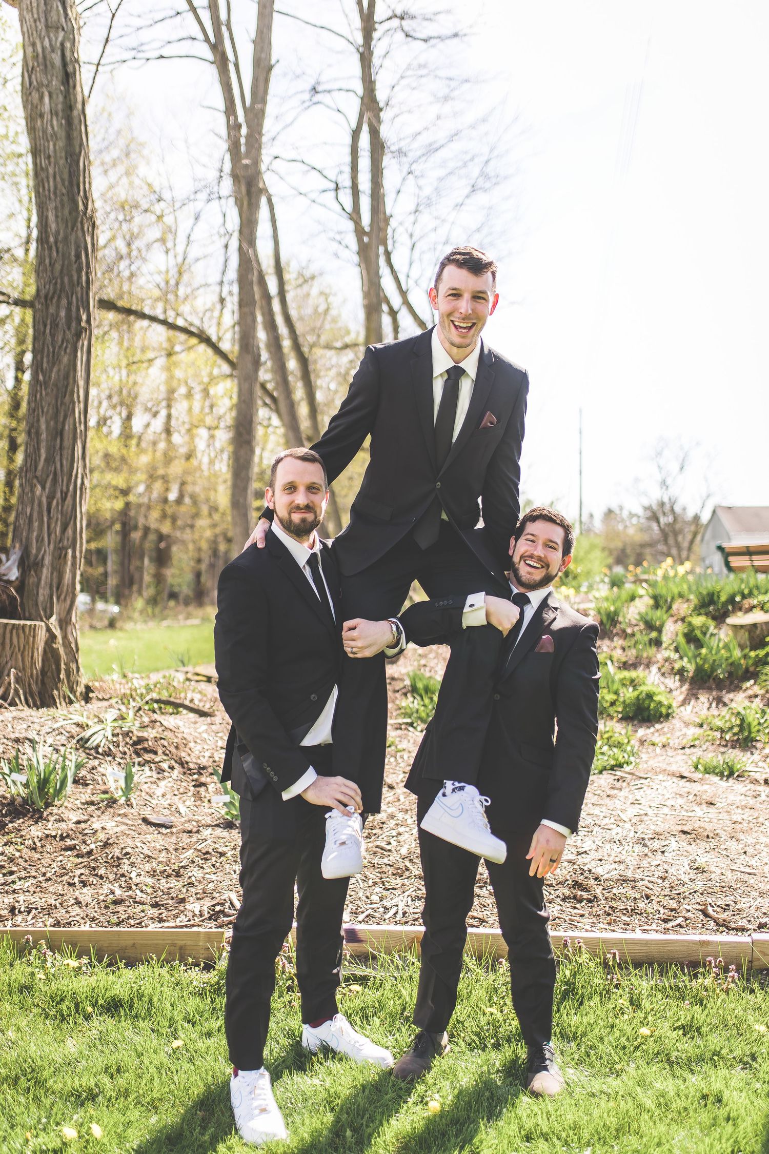 Groomsmen showing off their white sneakers in a playful outdoor photo.