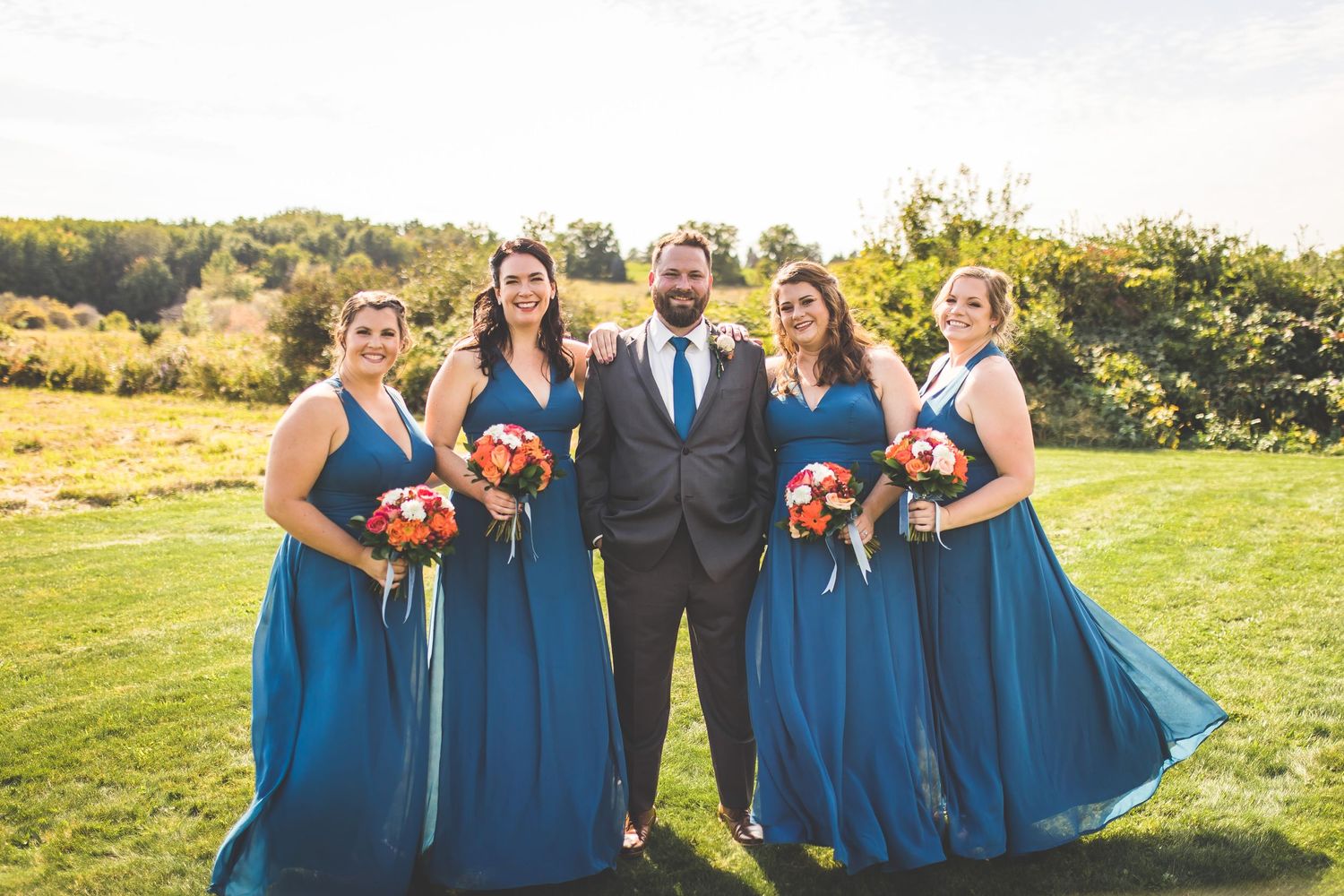 Bridal party in navy blue and gray poses together on rolling hills.