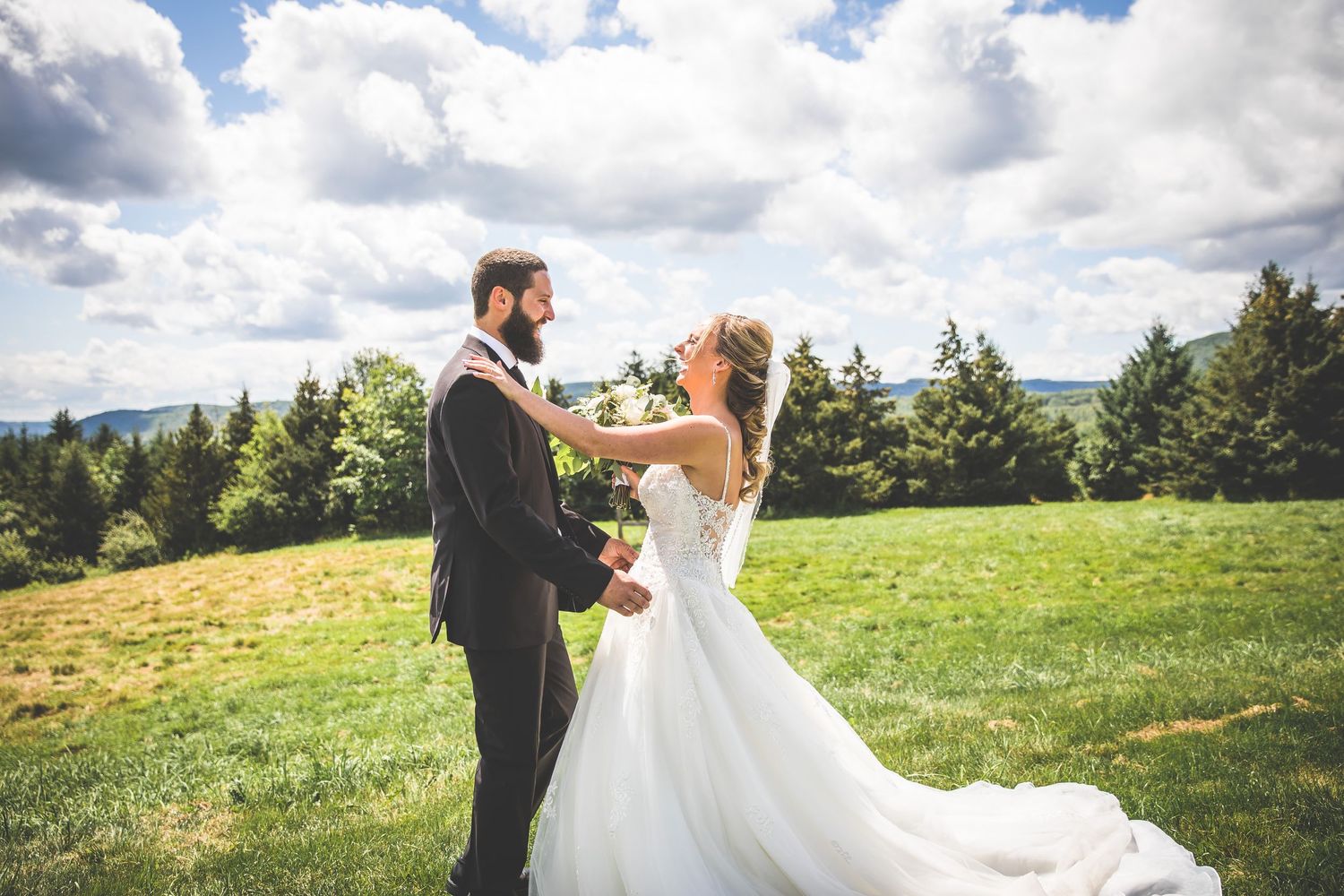 Newlyweds embracing in green field under dramatic cloudy sky.