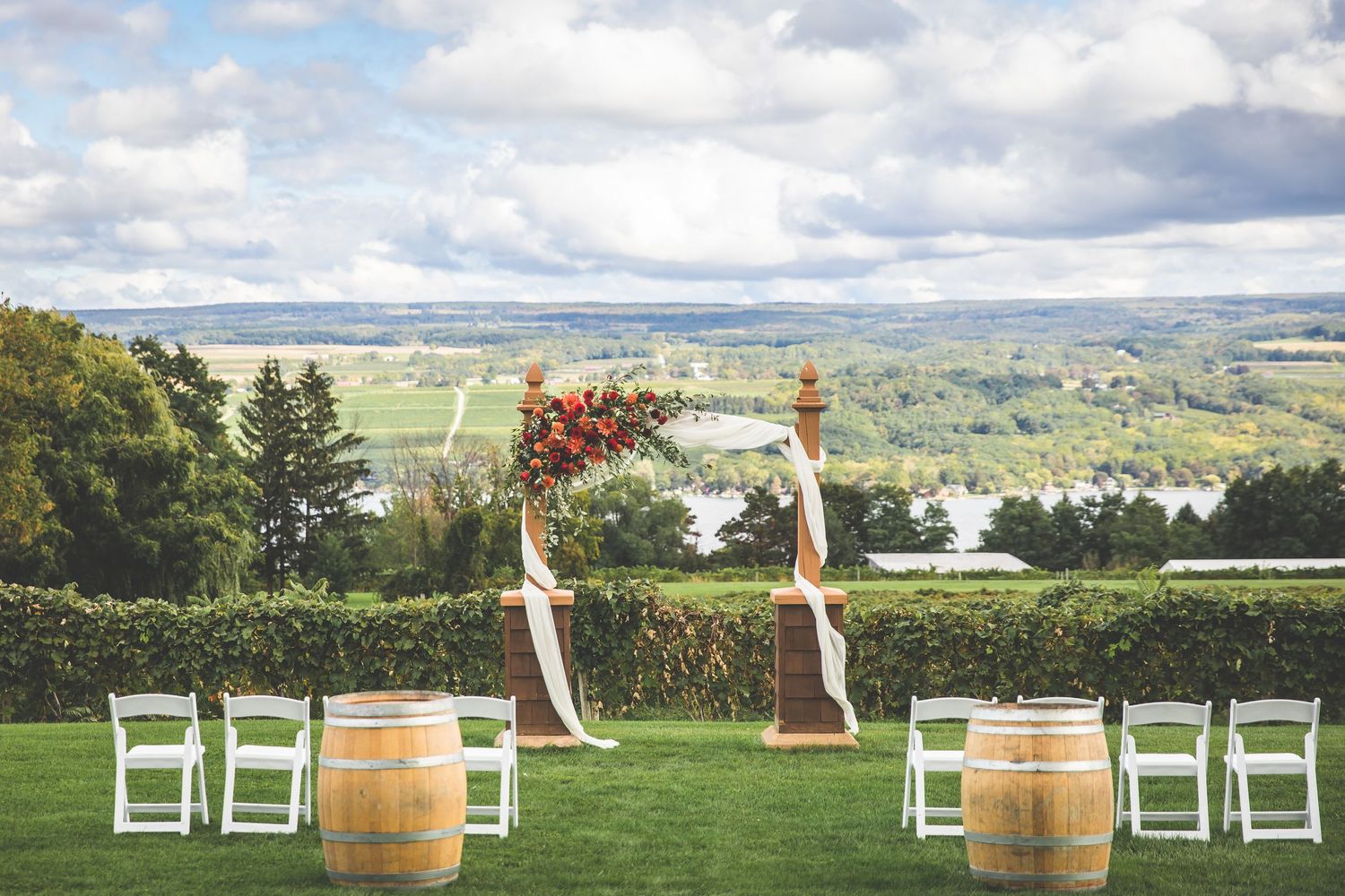 Outdoor wedding ceremony setup with white chairs and wine barrels against mountain backdrop.