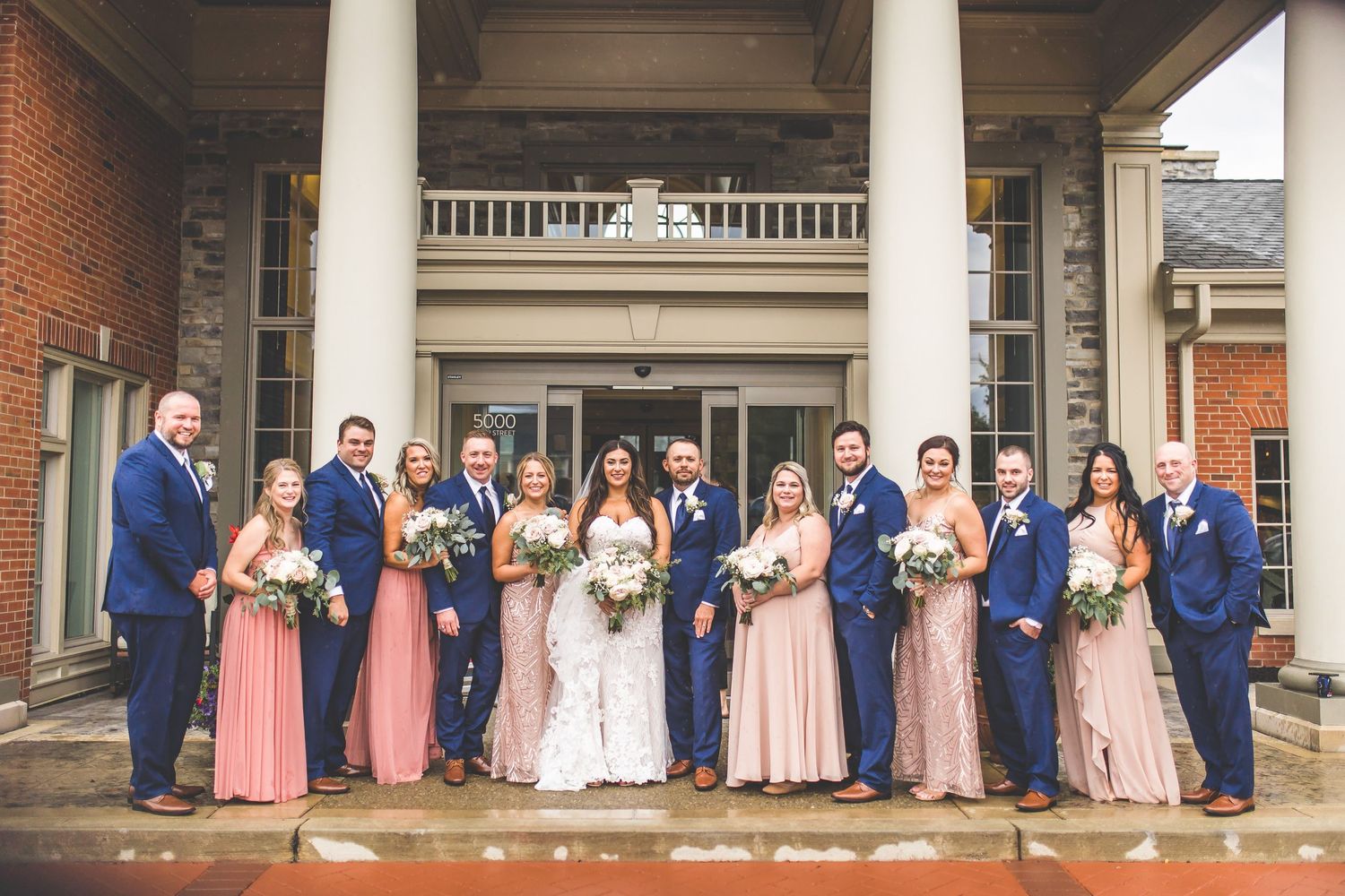 Wedding party lined up on classic brick building porch with white columns.