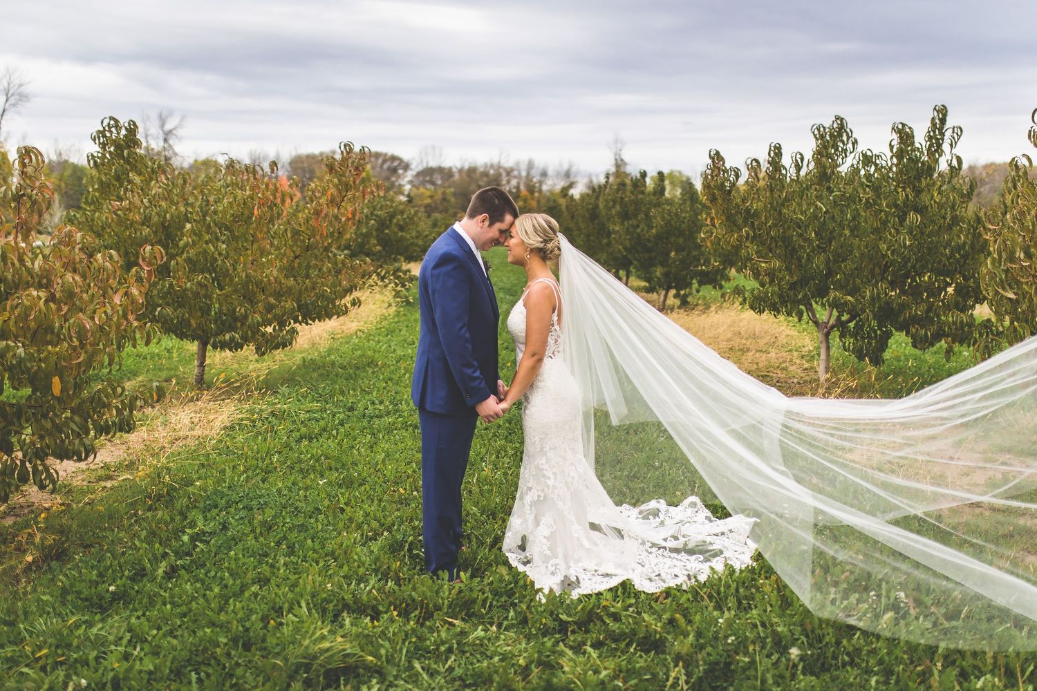Flowing cathedral veil creates dramatic wedding photos in natural outdoor setting.