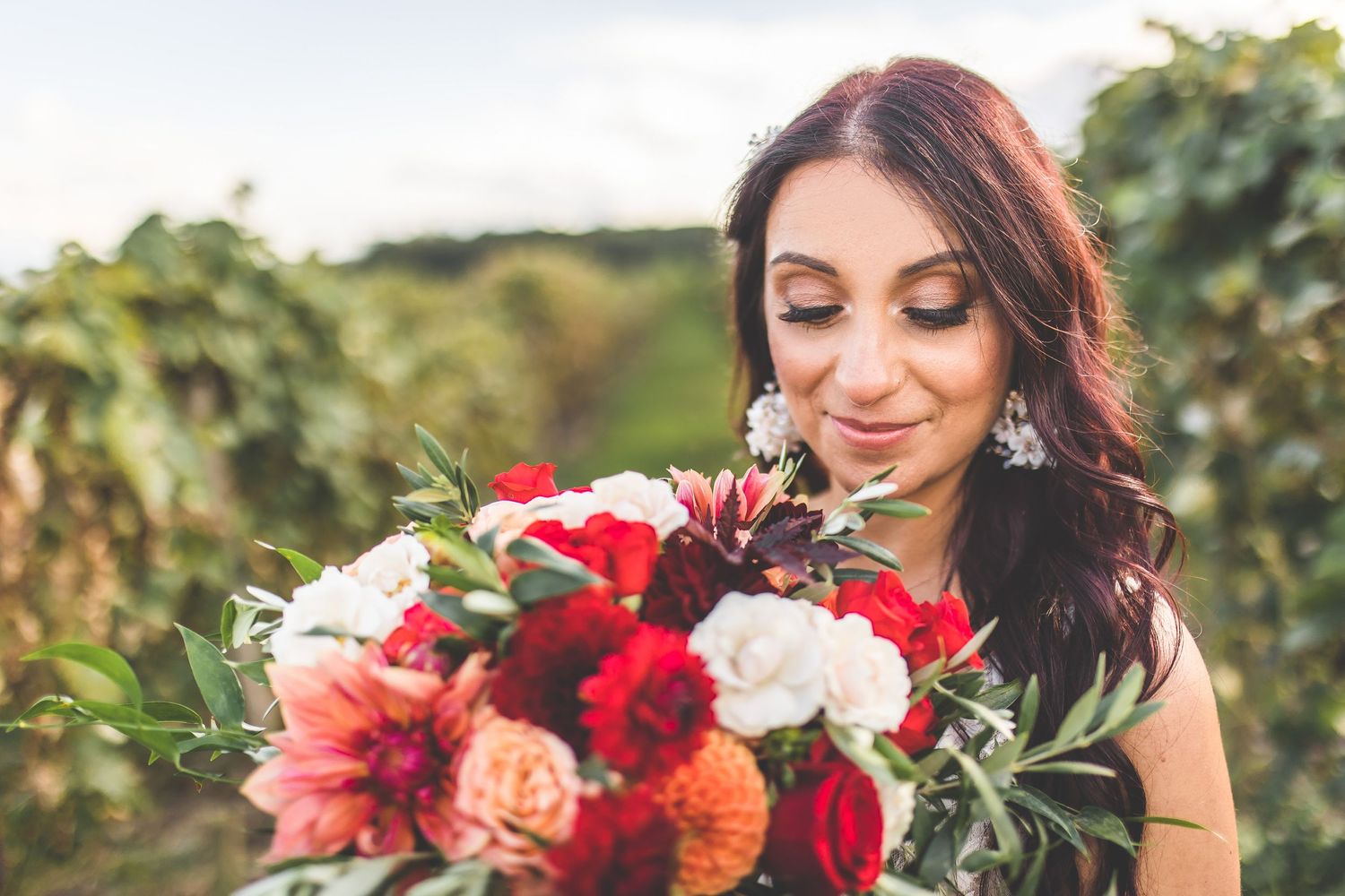 Vibrant red and coral floral bouquet with greenery against a vineyard backdrop.