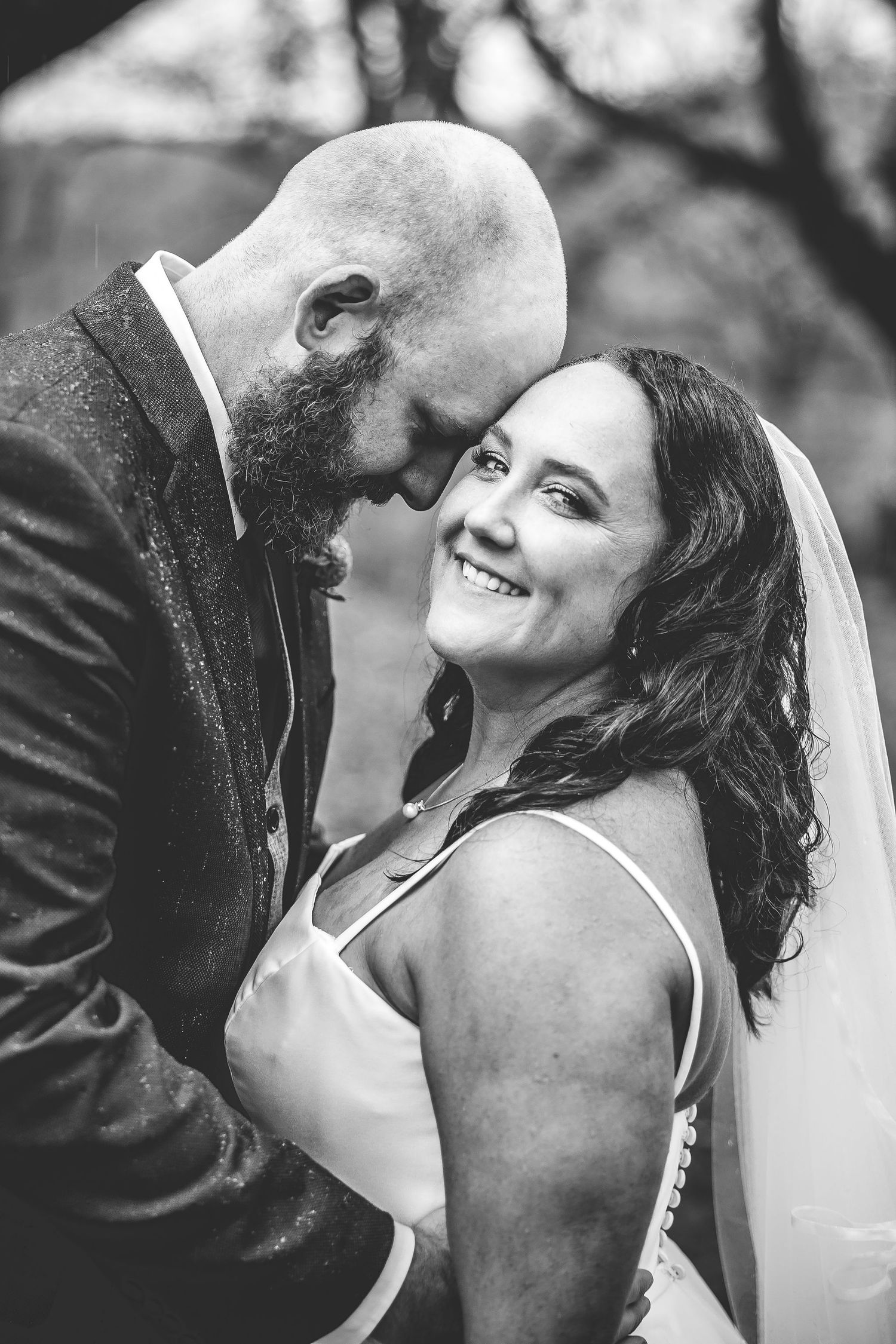Black and white close-up captures joyful laughter between newlyweds during outdoor photoshoot.