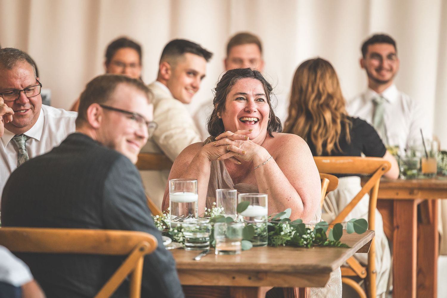 Wedding reception guests share joyful laughter around a decorated dining table.