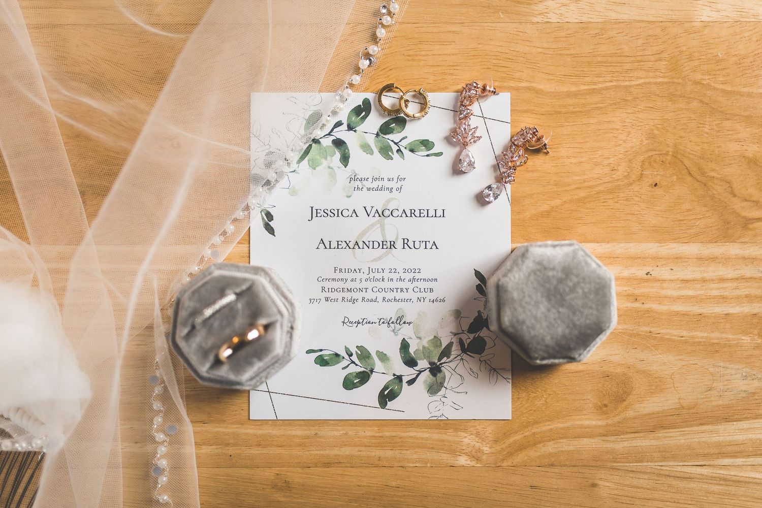 Wedding invitation with floral design and greenery details on wooden surface.