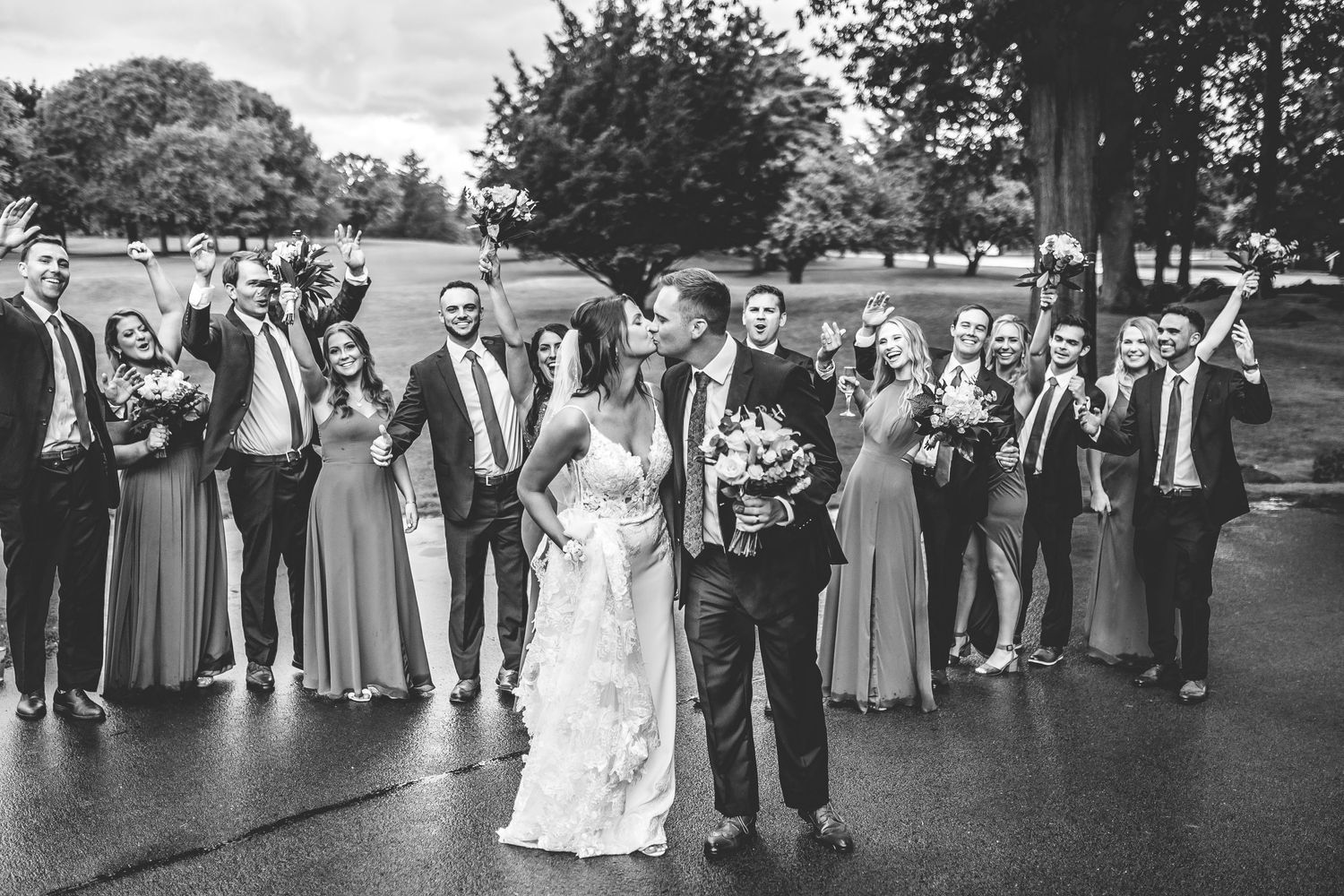 Black and white photo of wedding party lined up on grass with trees in background.