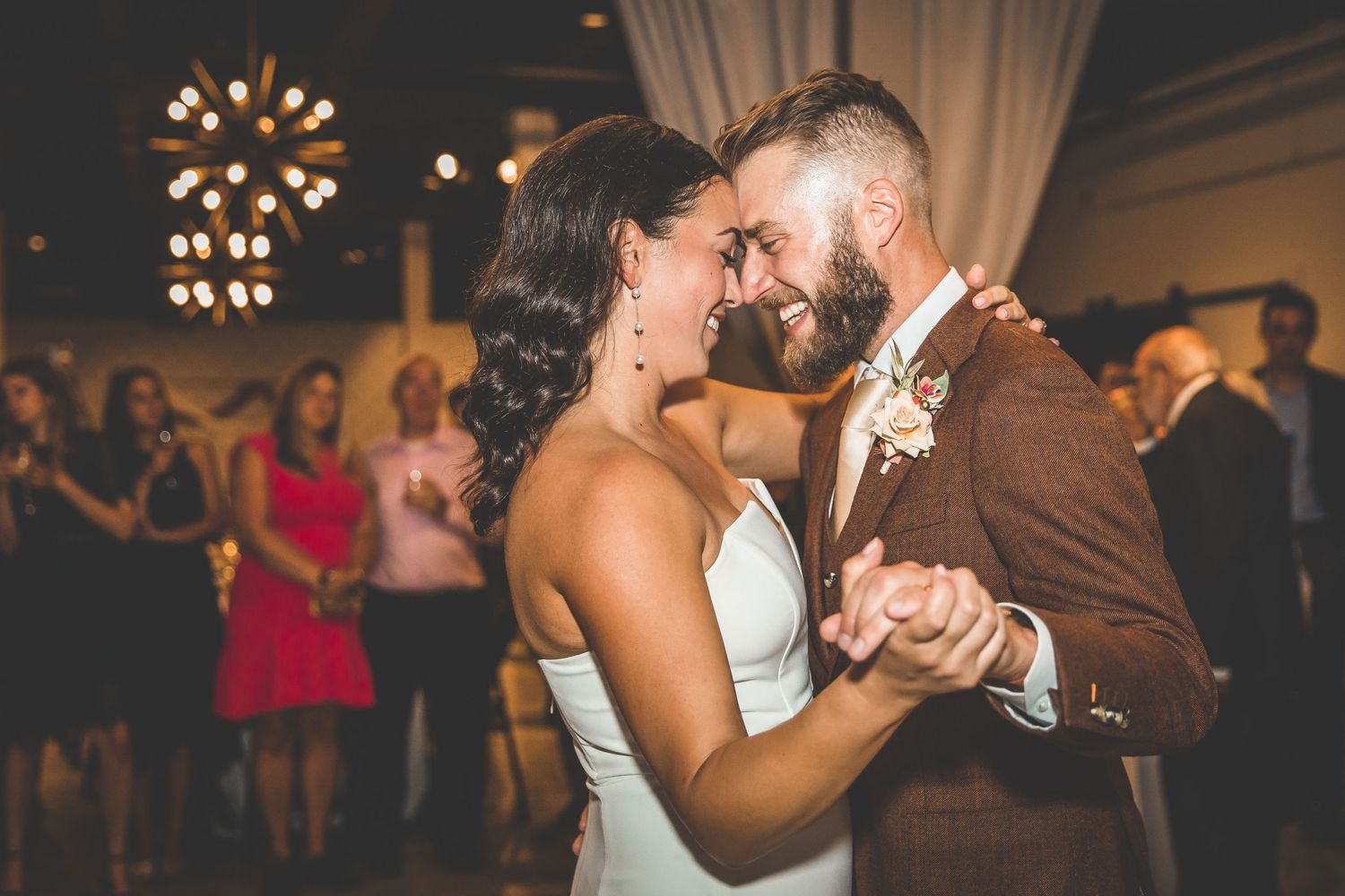 Newlyweds share an intimate dance moment under warm chandelier lighting at their reception.