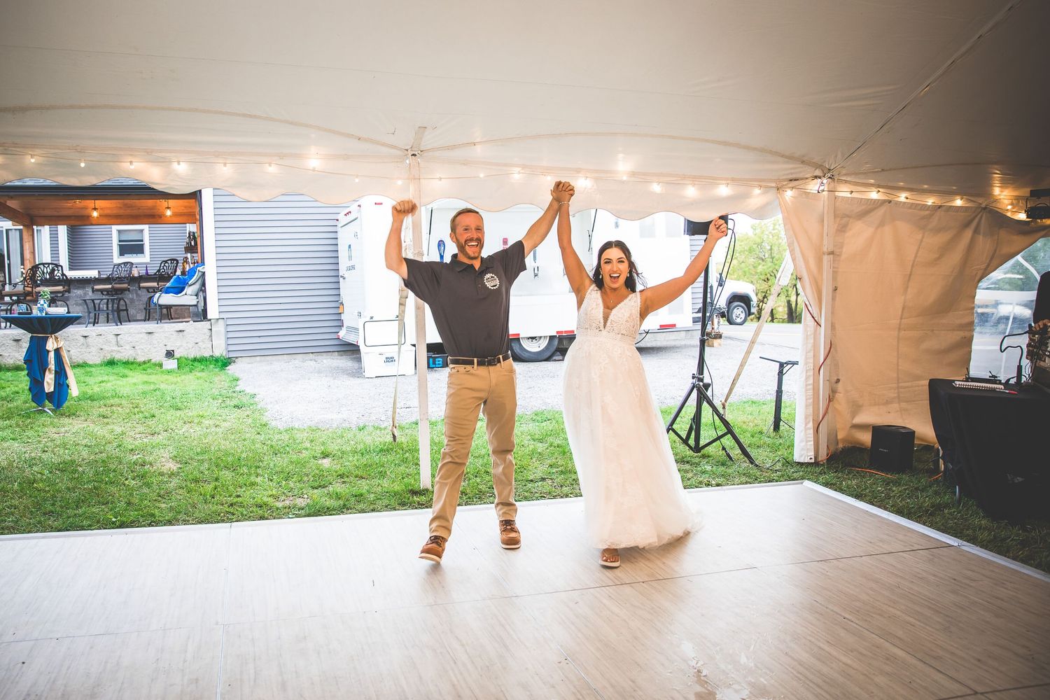 Wedding reception dance floor under white tent with string lights and joyful celebration.
