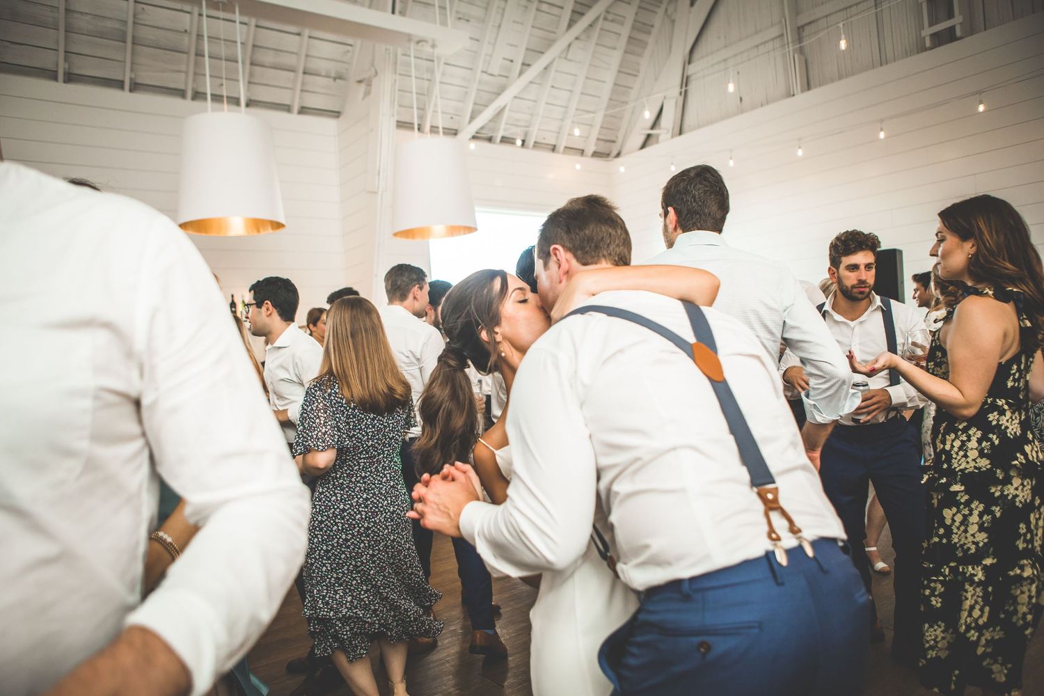 Wedding guests dance and celebrate on a wooden dance floor at an indoor reception venue.