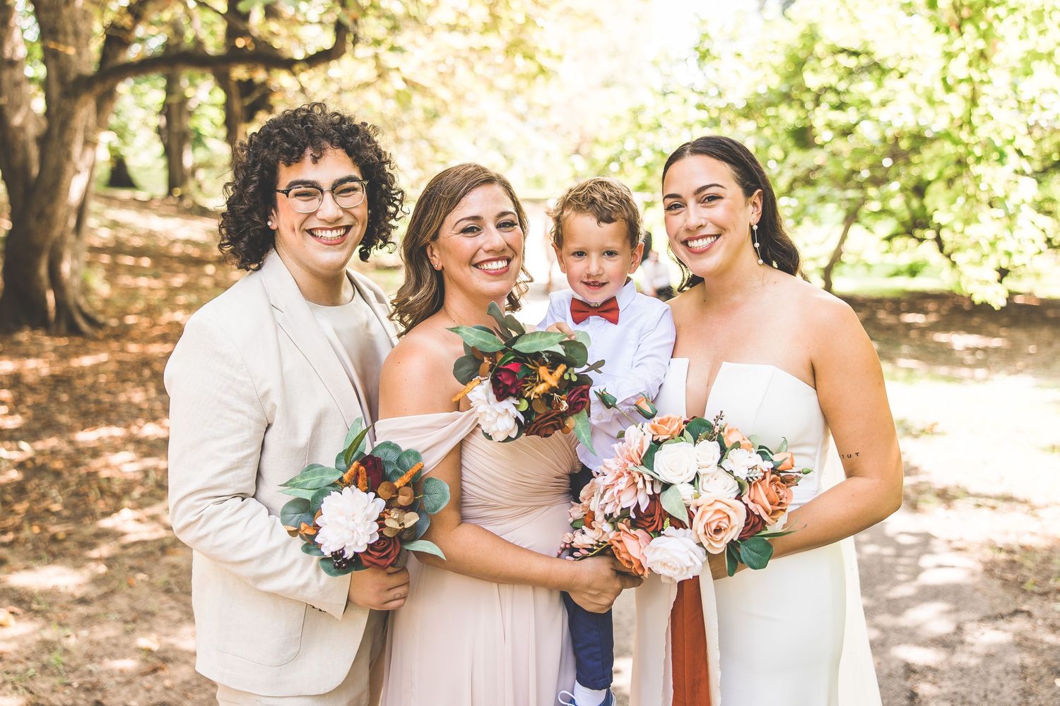 Wedding party members hold floral bouquets while posing in garden setting.