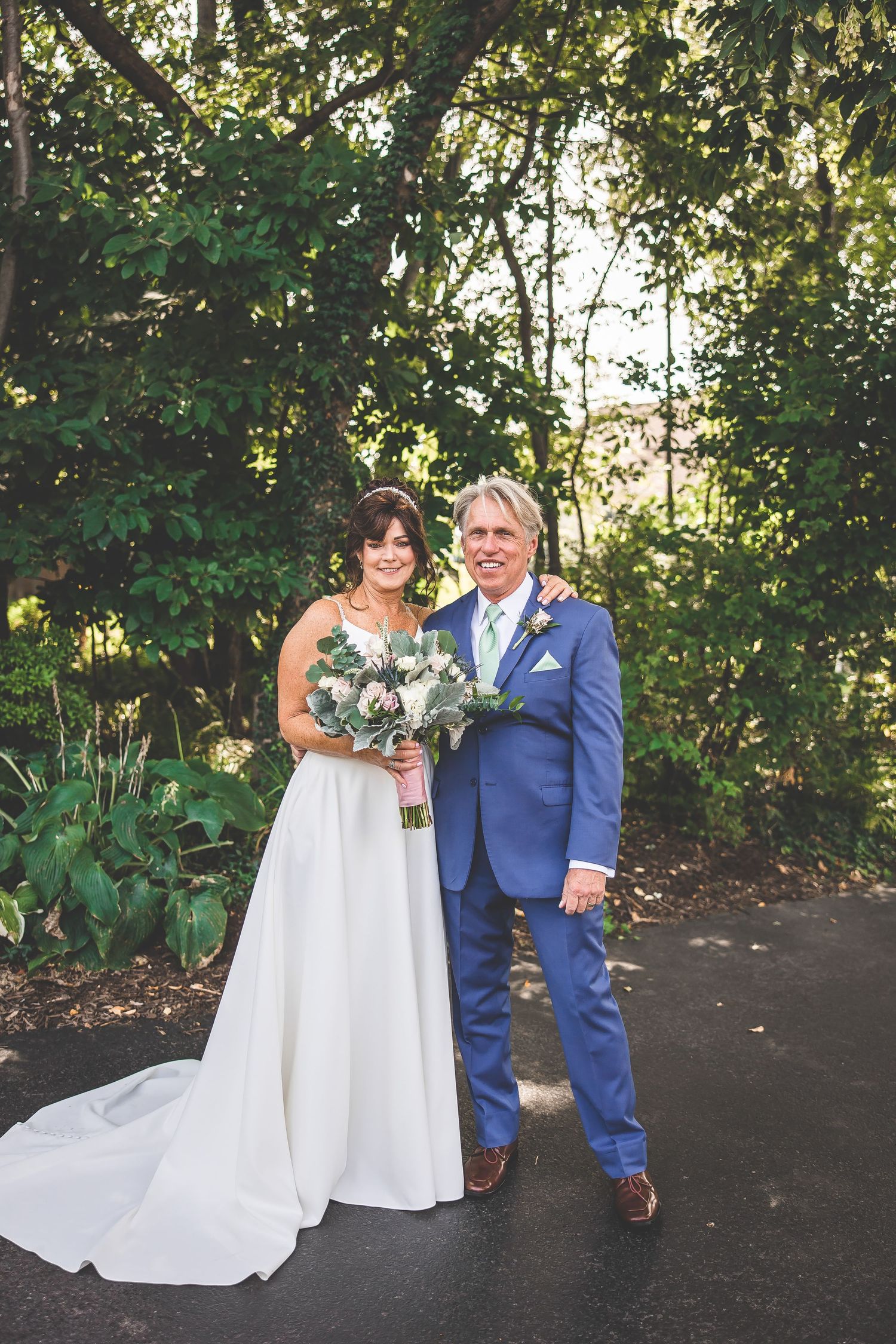 Wedding couple poses together on garden path surrounded by greenery.