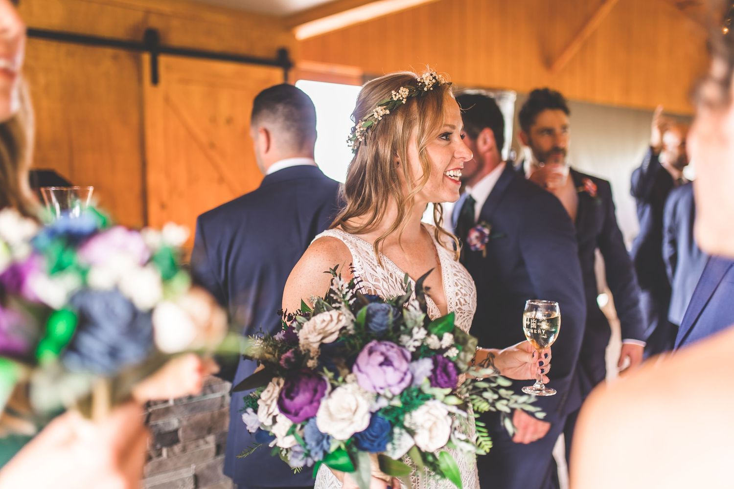 Wedding celebration with purple floral bouquets and natural lighting in rustic venue.
