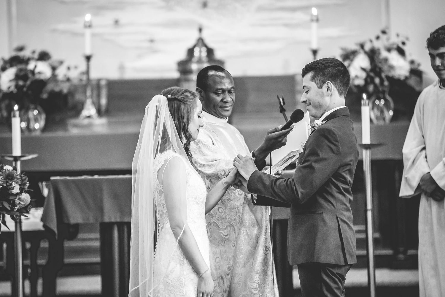 Black and white photo of a wedding ceremony with couple exchanging rings at church altar.